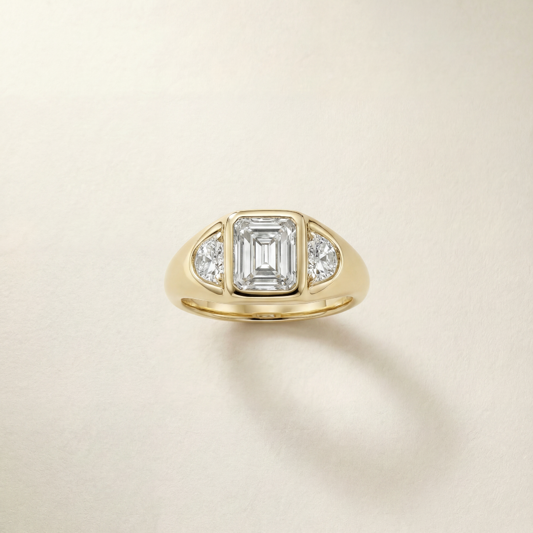 Gold ring with a central emerald-cut diamond and smaller diamonds on a beige background