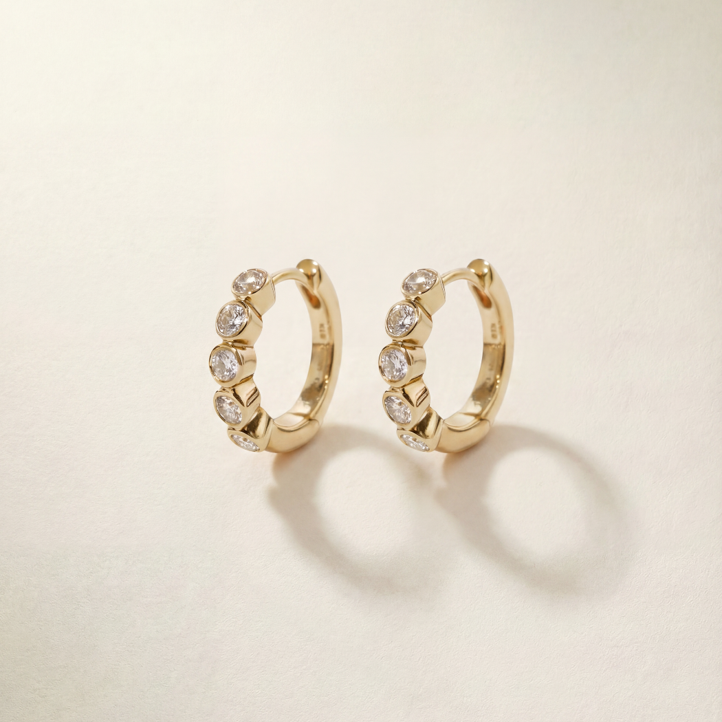 Gold hoop earrings with embedded stones on a beige background