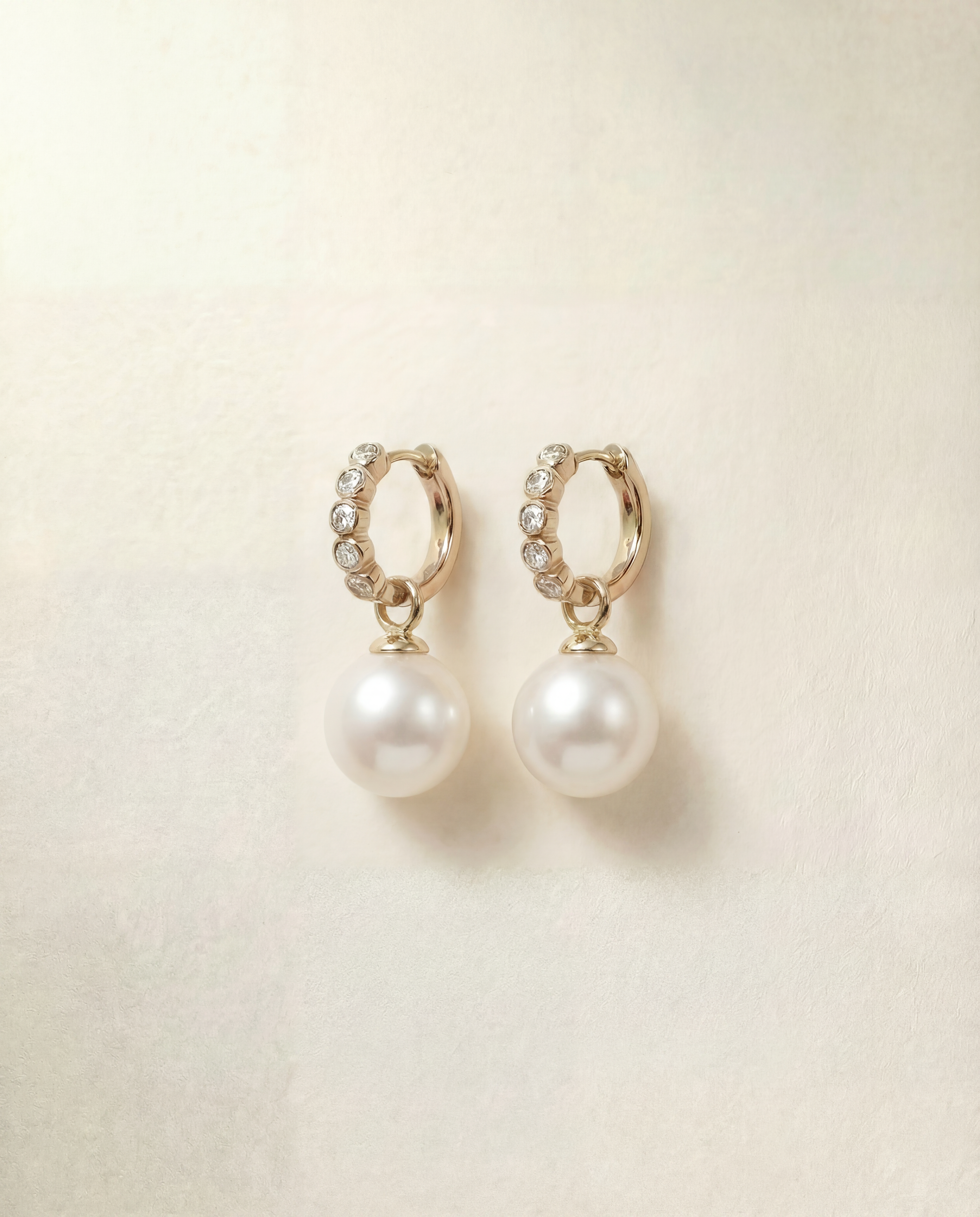 Pair of pearl earrings with gold hoop accents on a beige background