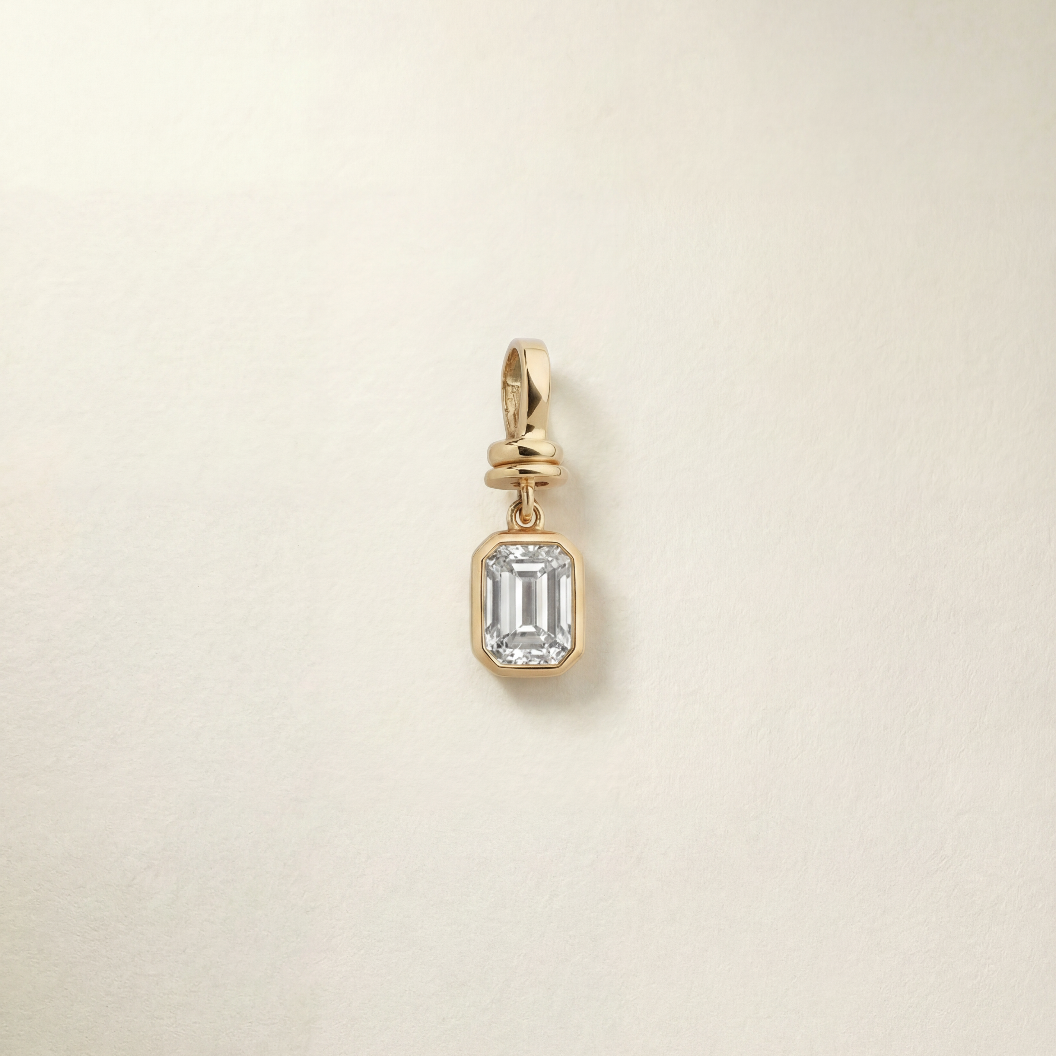 Gold pendant with a emerald diamond on a beige background