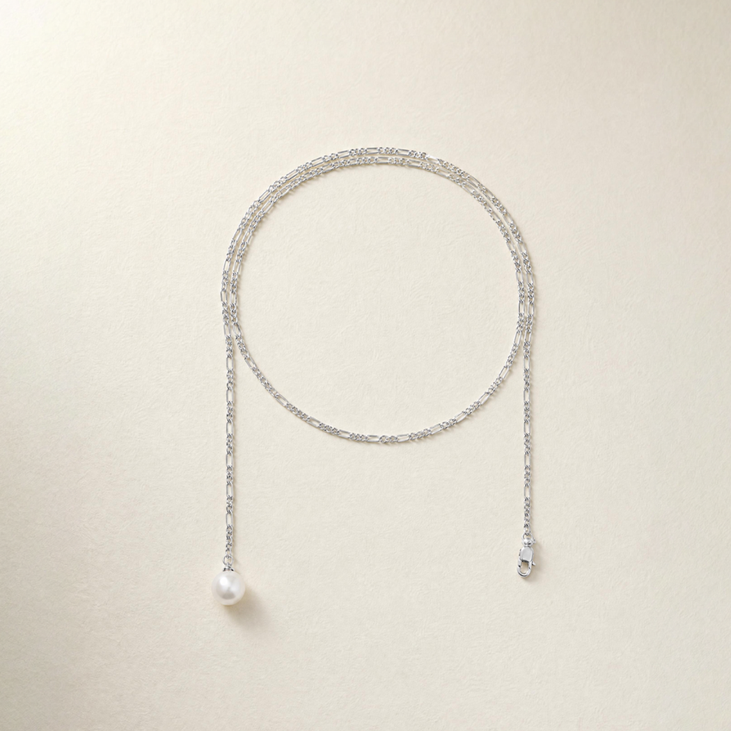 A delicate silver chain necklace with a pearl drop, on a light beige background.