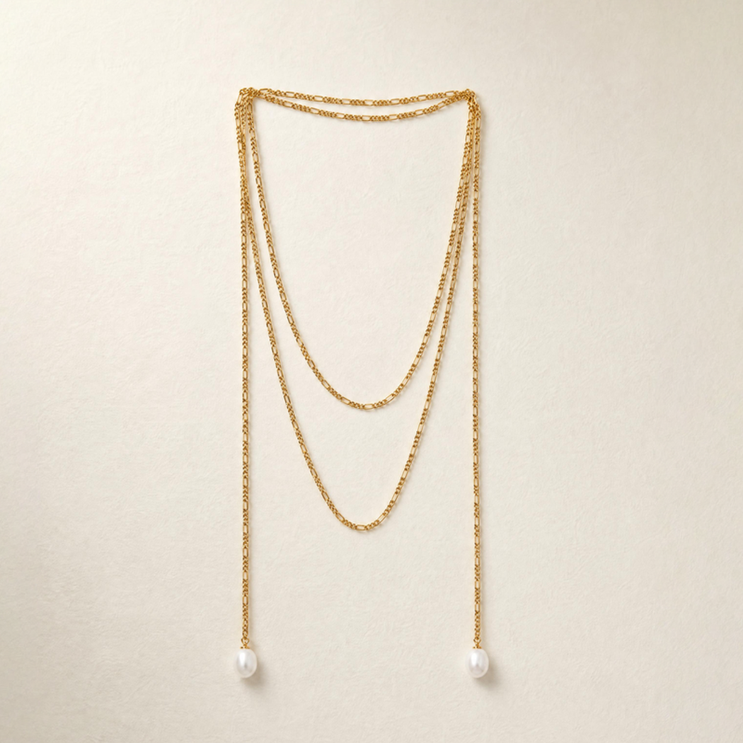 A gold-toned multi-layered drape necklace with south sea pearls, displayed against a light beige textured background.