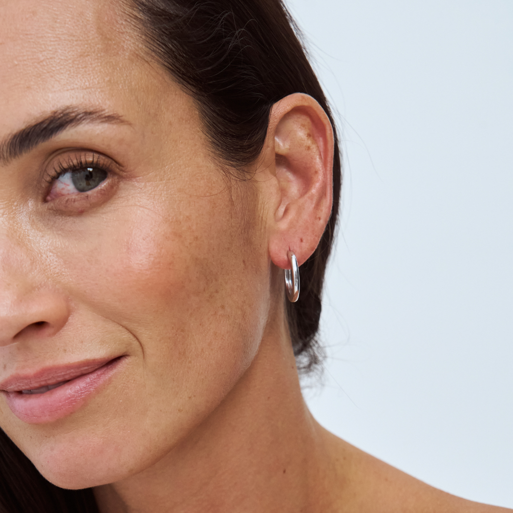 Close-up of an ear wearing a 9k yellow gold hoop earring on a light background