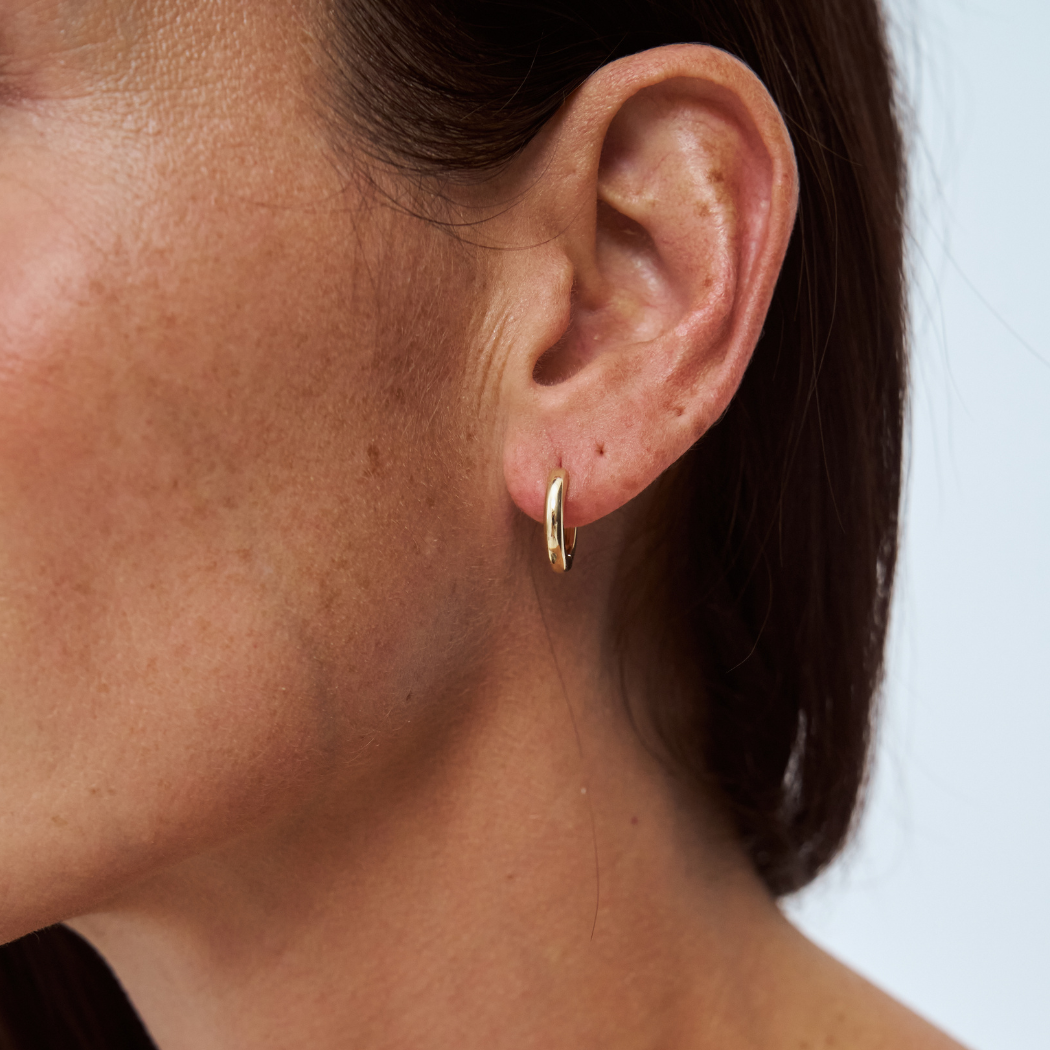 Close-up of a model wearing a small, solid gold hoop earring.