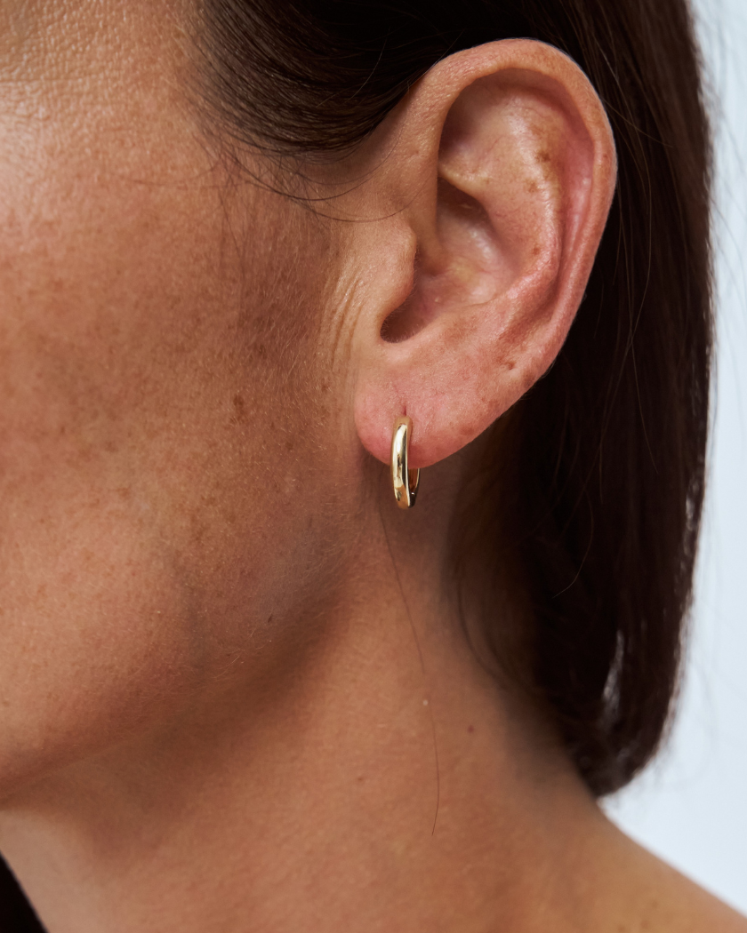 Close-up of a person wearing a 9k yellow gold hoop earring against a neutral background