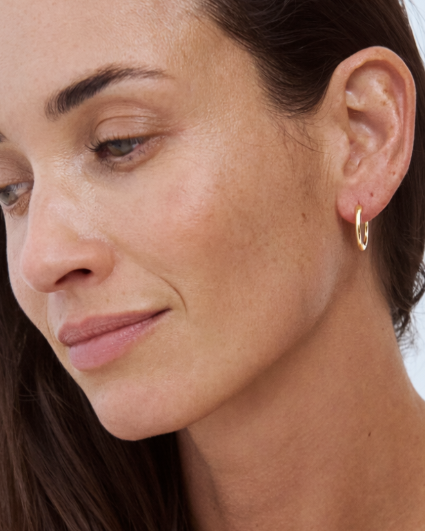 Close-up of a woman wearing a 9k yellow gold hoop earring against a light background