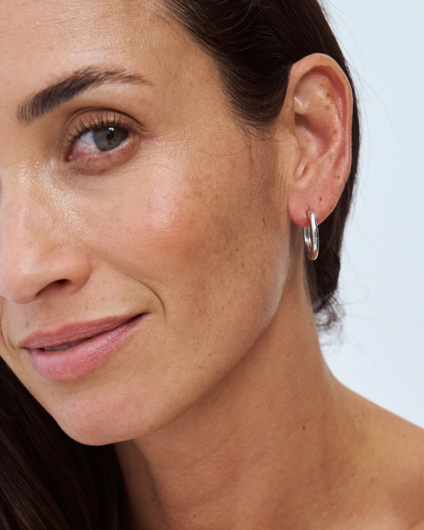 Close-up of a woman wearing a 9k white gold hoop earring against a light background