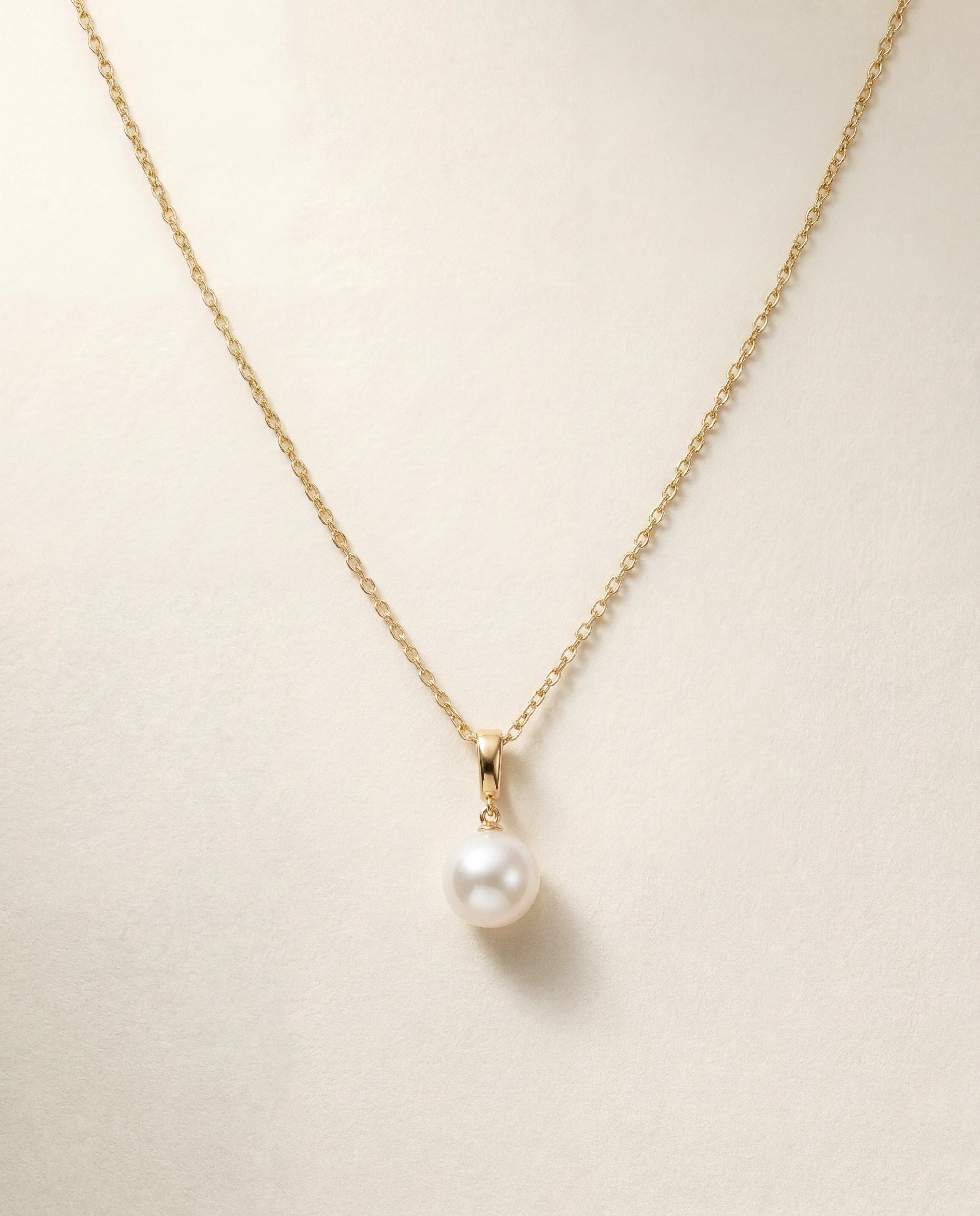 Pearl necklace on a gold chain against a beige background