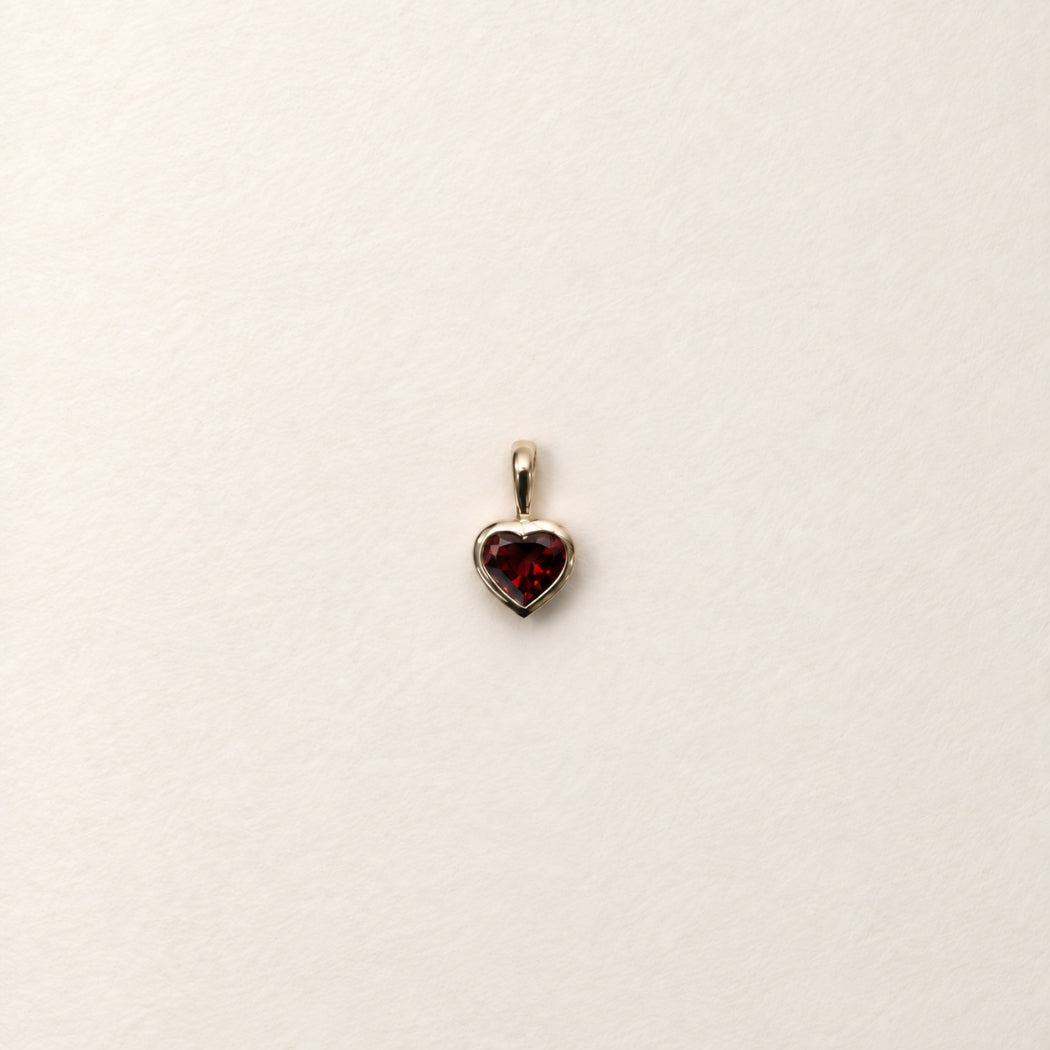 A red garnet heart-shaped pendant charm, bezel set in 9k yellow gold