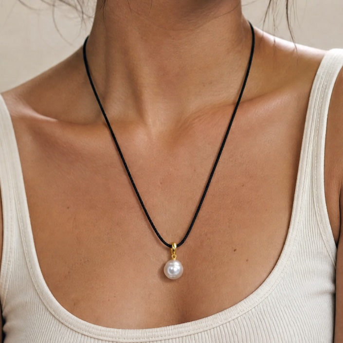 Woman wearing a necklace with a pearl pendant against a neutral background