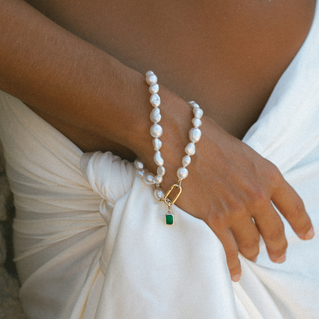 Up close of wrist wearing handmade South Sea Keshi pearl bracelets with 9k solid gold clasp with emerald charm.
