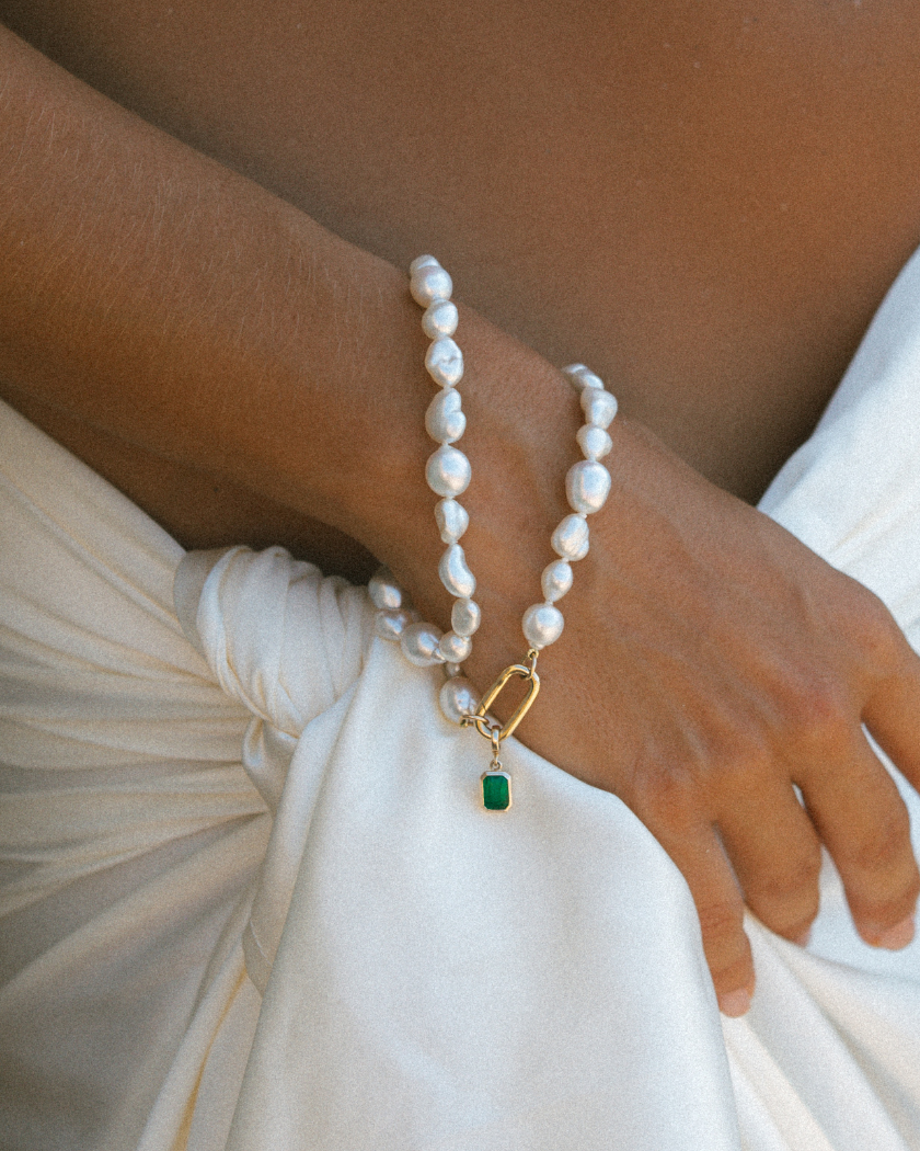 Up close of wrist wearing handmade South Sea Keshi pearl bracelets with 9k solid gold clasp with emerald charm.