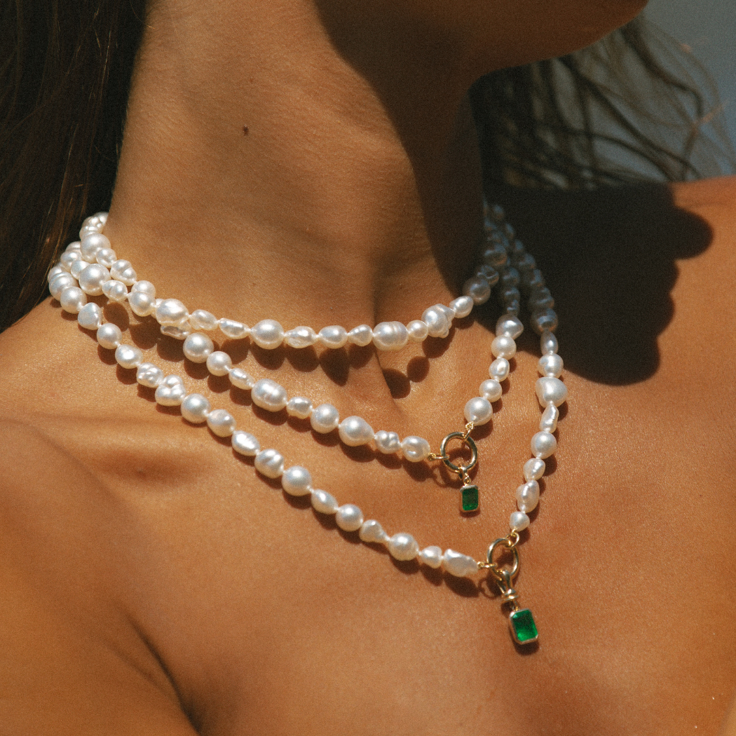 Layered doble row and single handmade South Sea pearl necklaces on neck with 9k solid gold clasp and emerald charms.