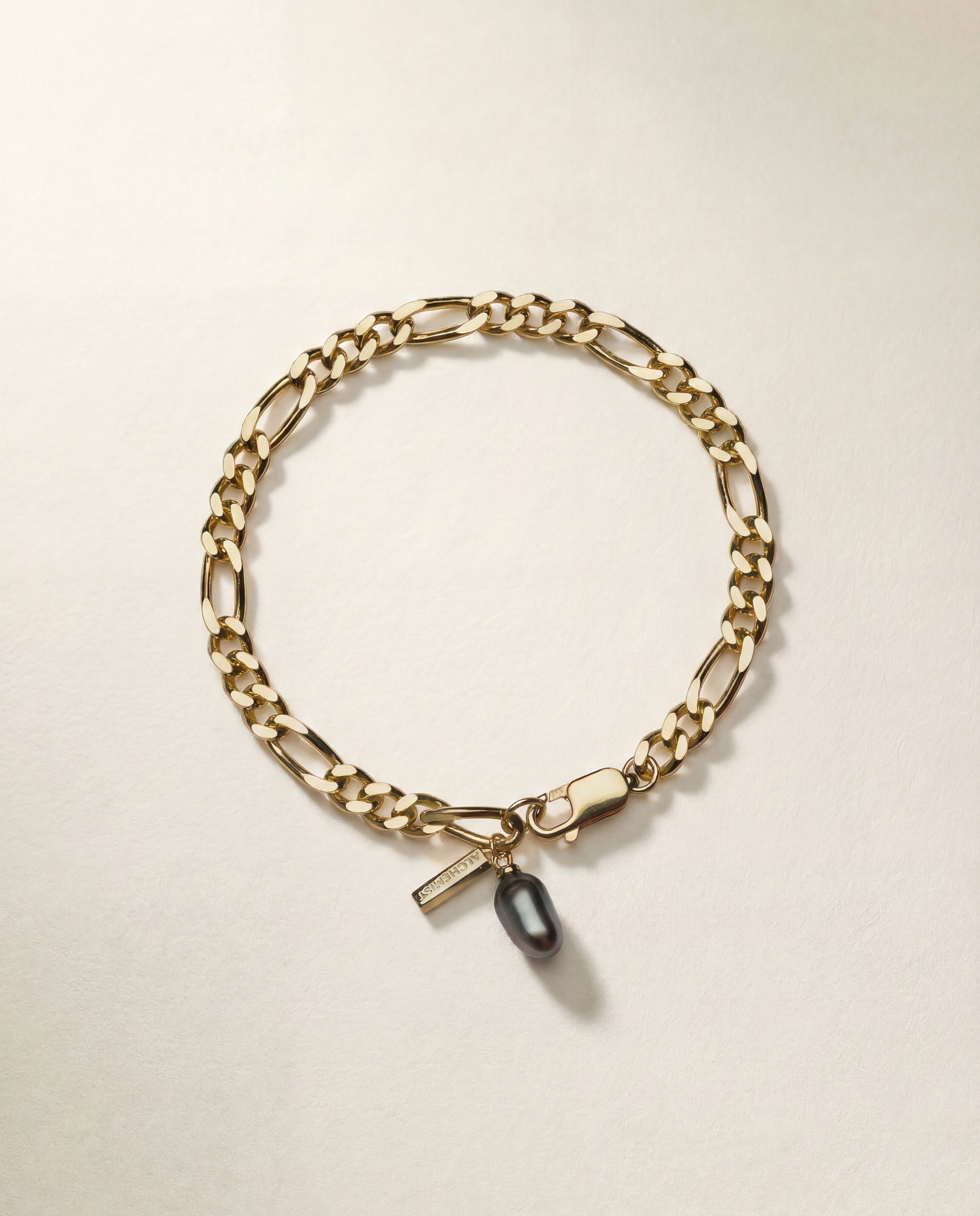 Gold chain bracelet with a tag and black pearl on a beige background