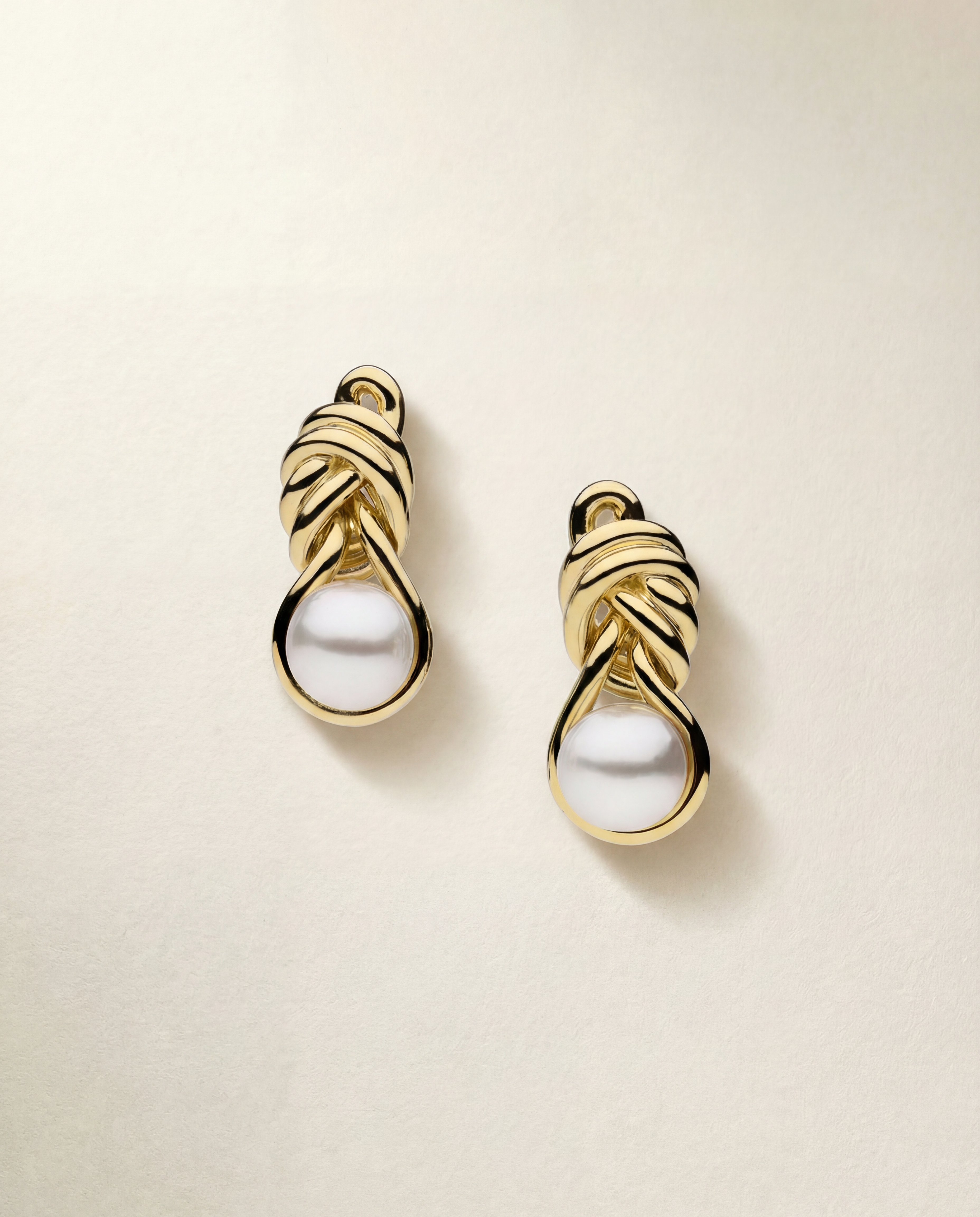 Pair of gold earrings with pearls on a beige background
