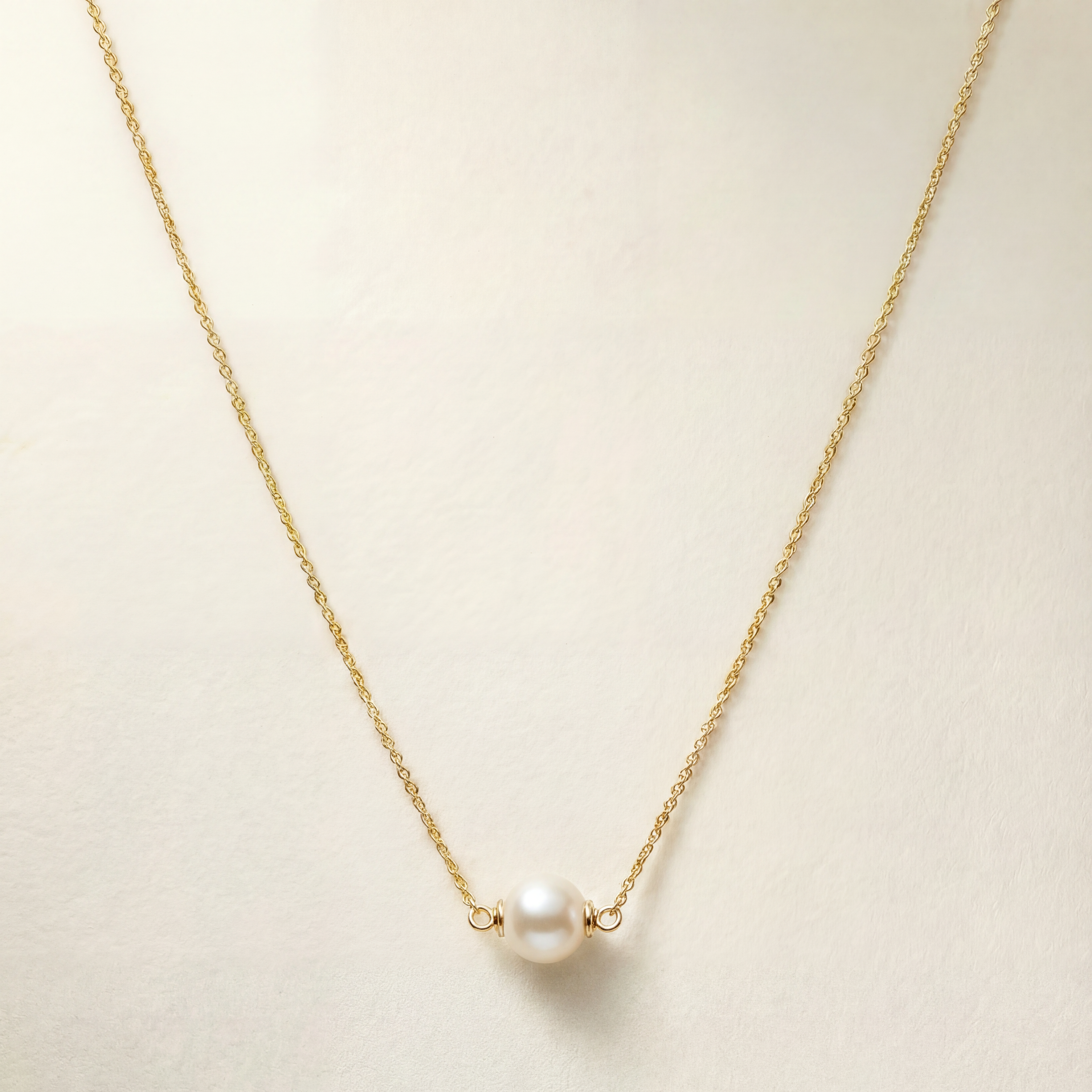 Gold necklace with a single pearl on a light beige background