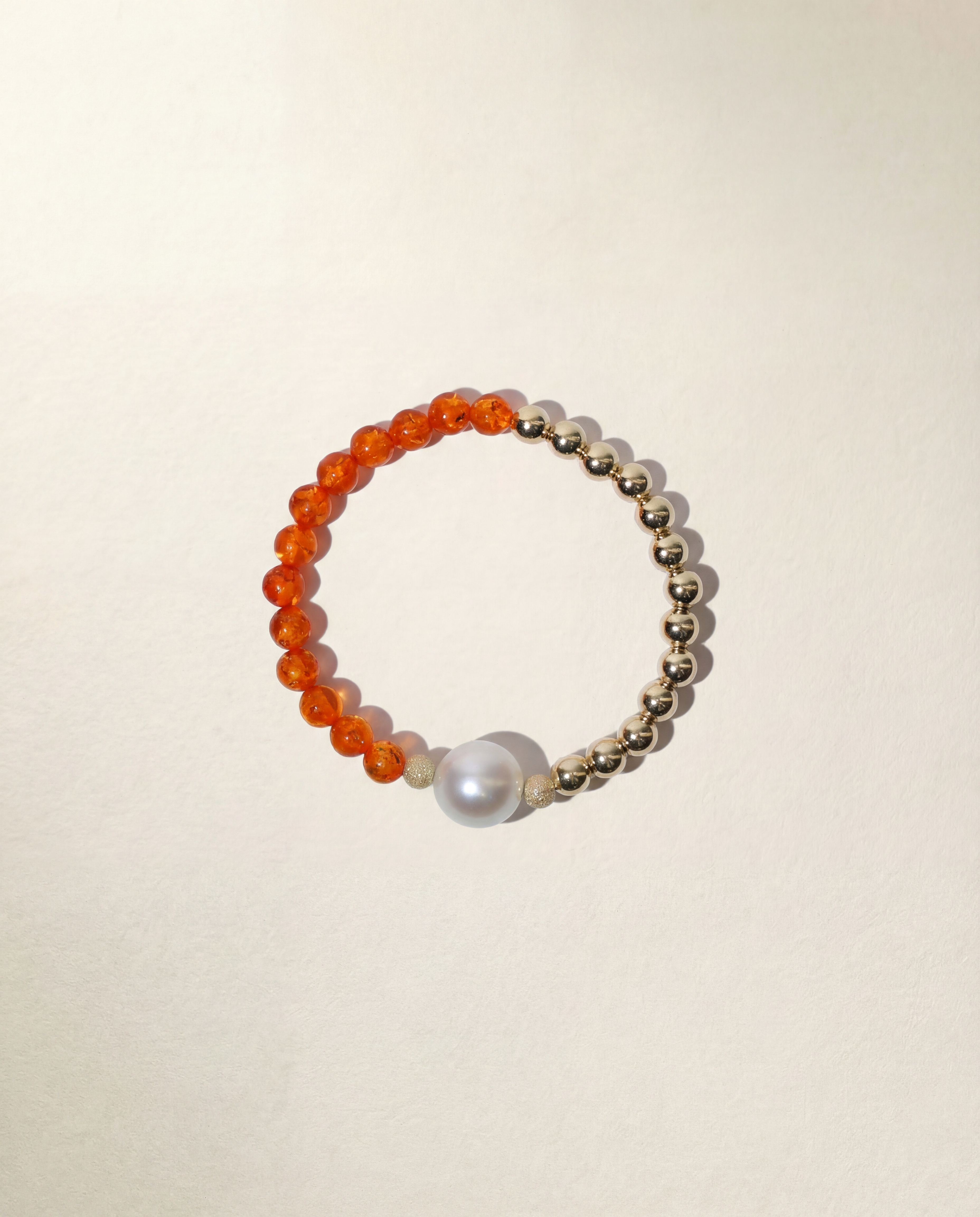 Bracelet with orange beads and a pearl on a beige background