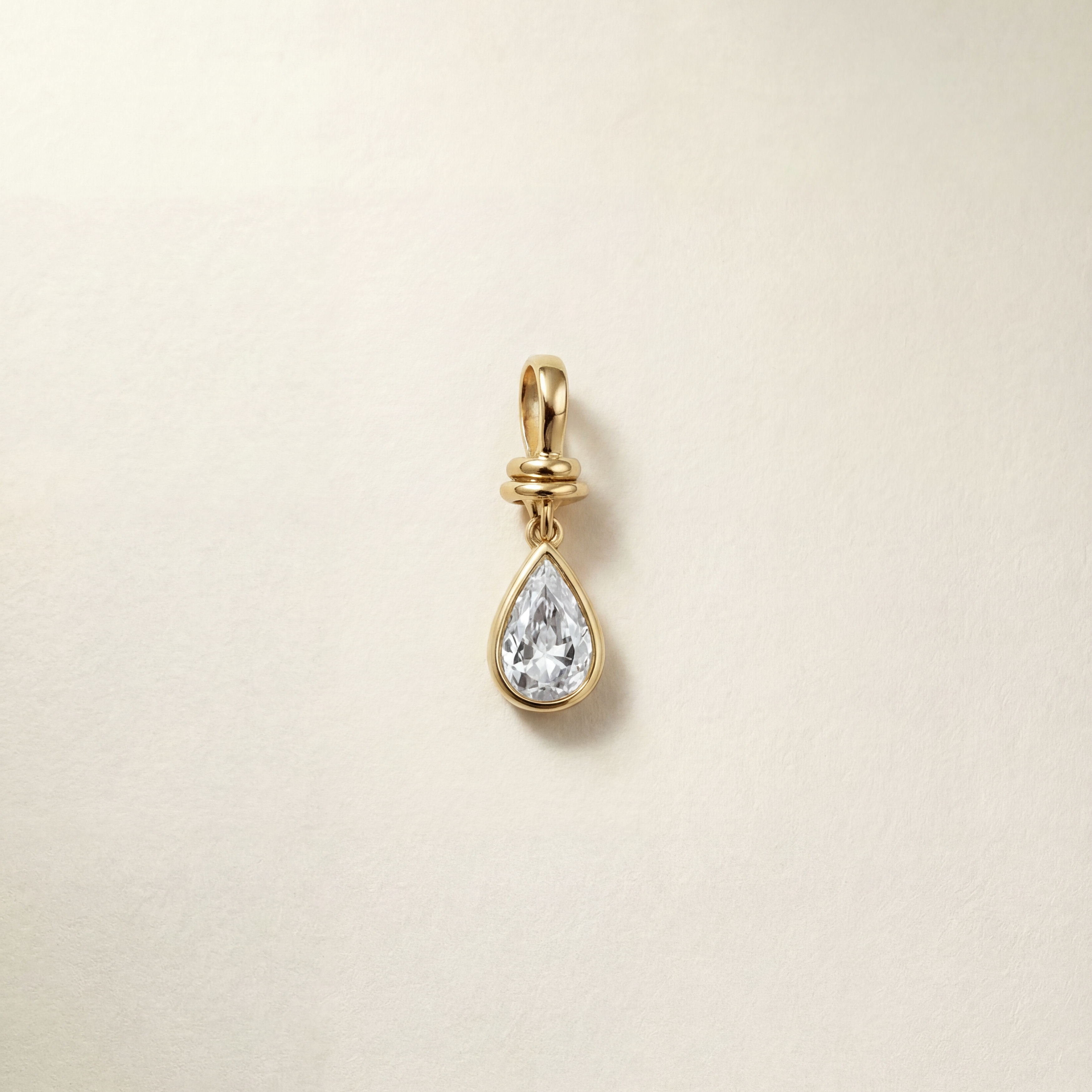 Gold teardrop-shaped pendant with a clear gemstone on a beige background