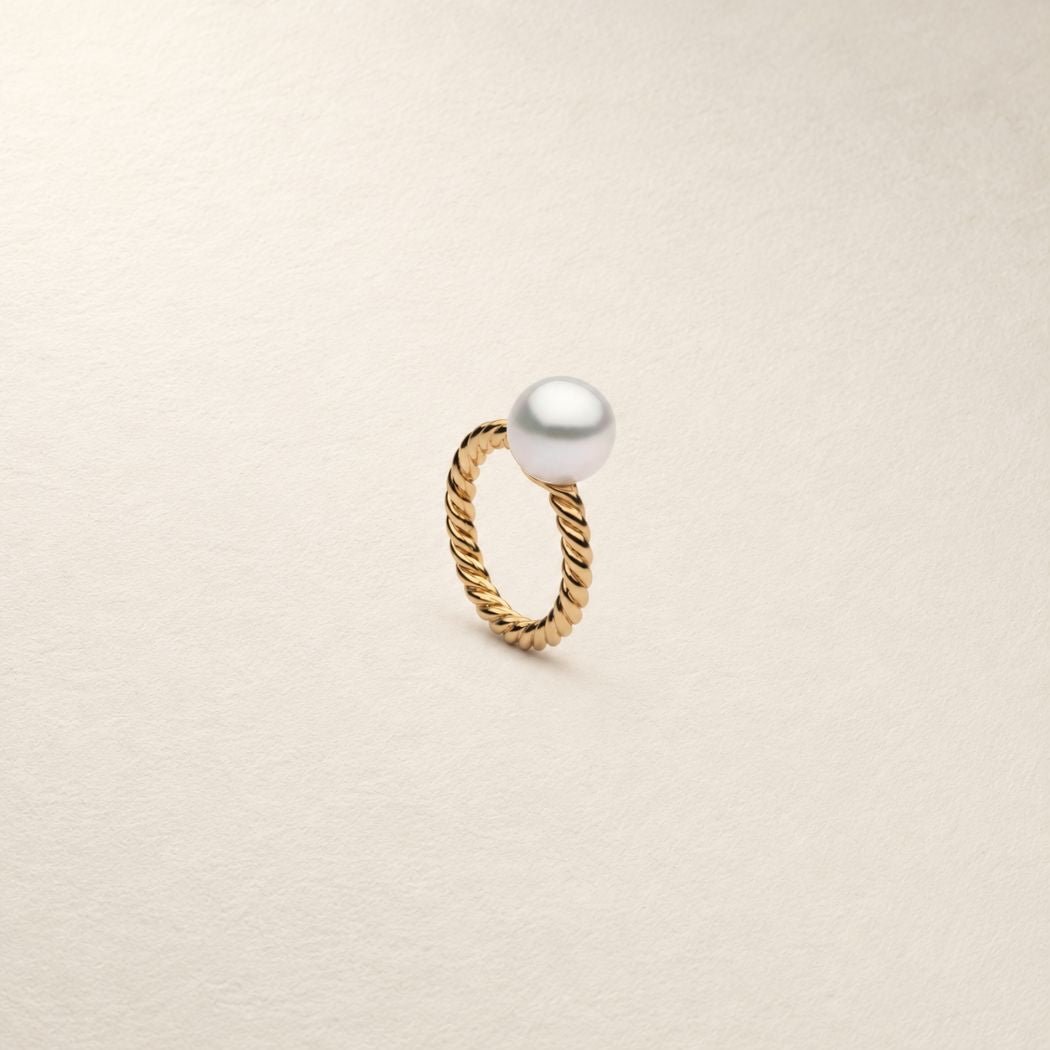 A gold ring with a twisted rope-style band and a single south sea white pearl at the top, photographed on a plain light background.