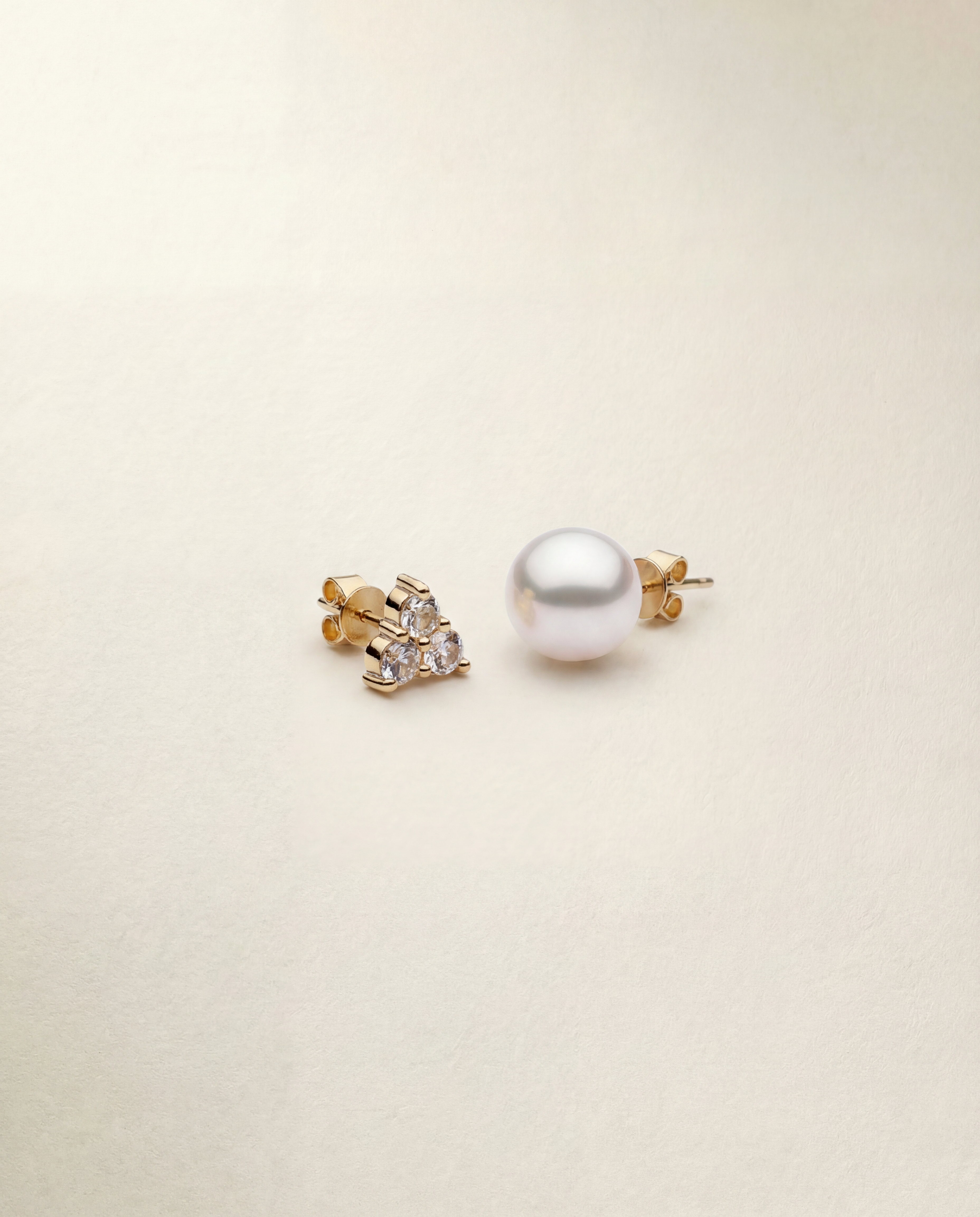 Pearl earring and gold earring with gemstones on a beige background