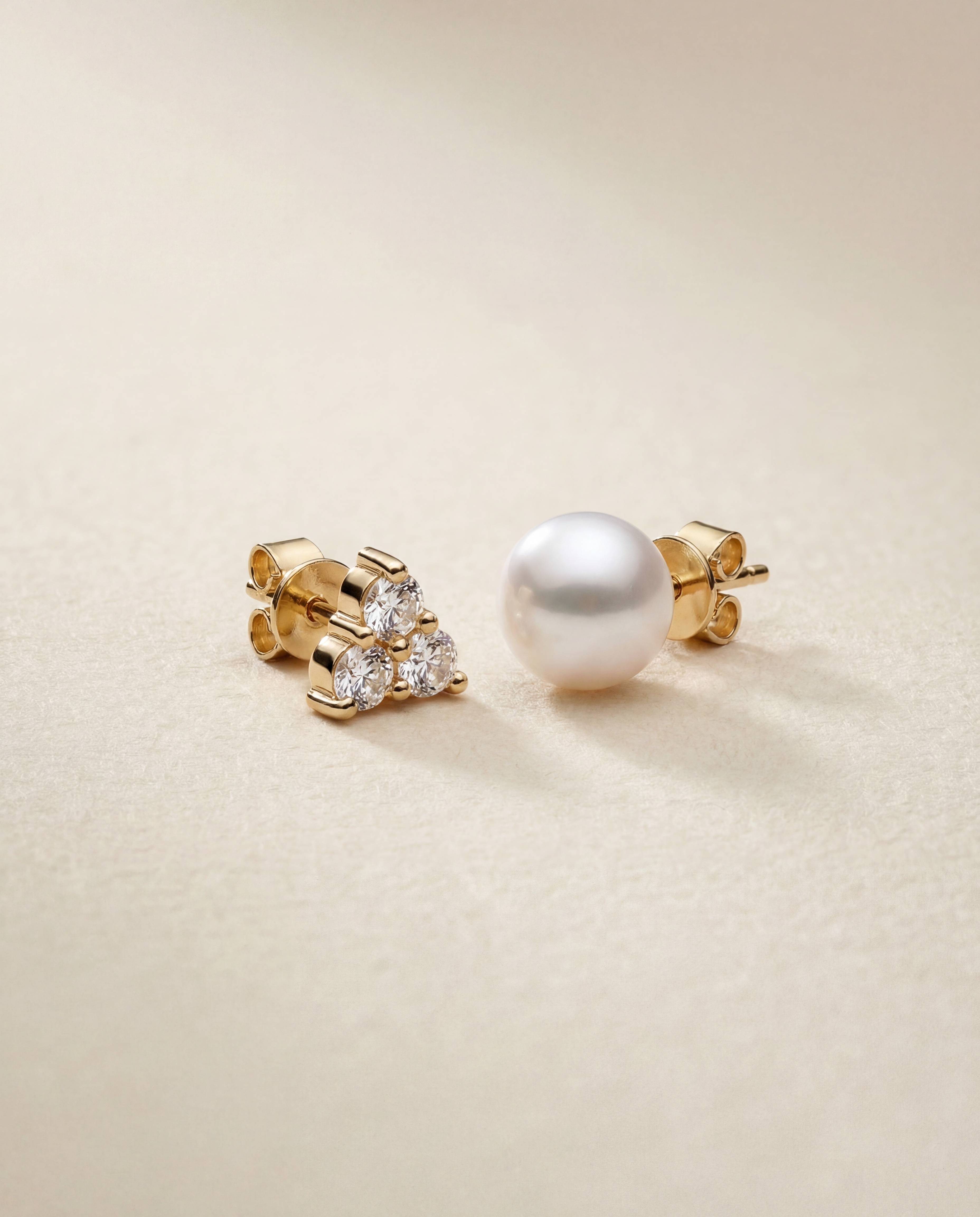 Gold earrings with a pearl and white sapphires on a beige background