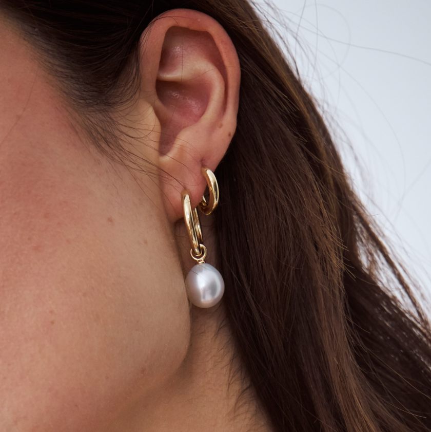 Close-up of an ear wearing a gold hoop earring with a south sea pearl charm.
