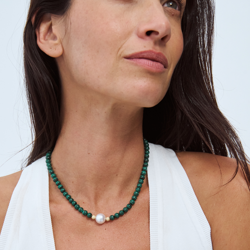 Woman wearing a malachite beaded necklace with a south sea pearl and 9k yellow gold clasp.