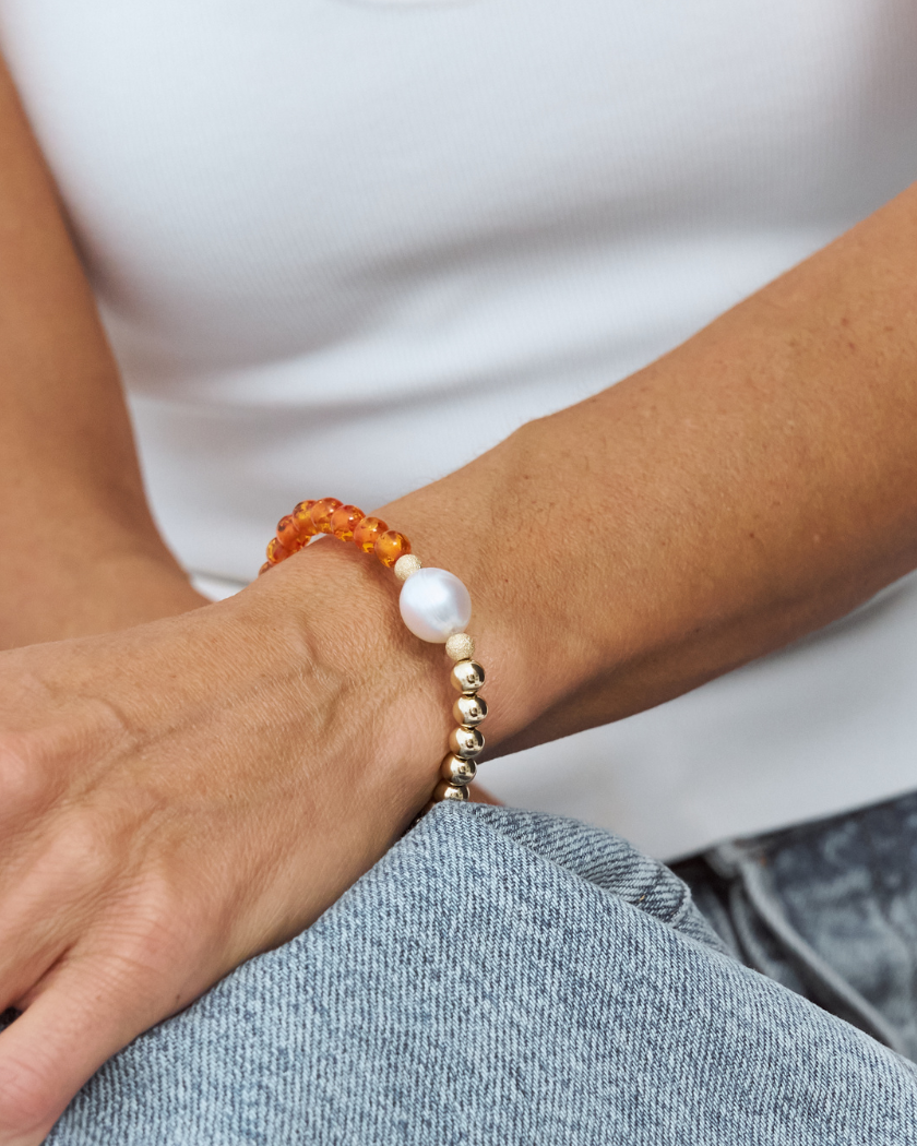 Close-up of a wrist, wearing a bracelet with a south sea pearl, amber and gold beads on a neutral background