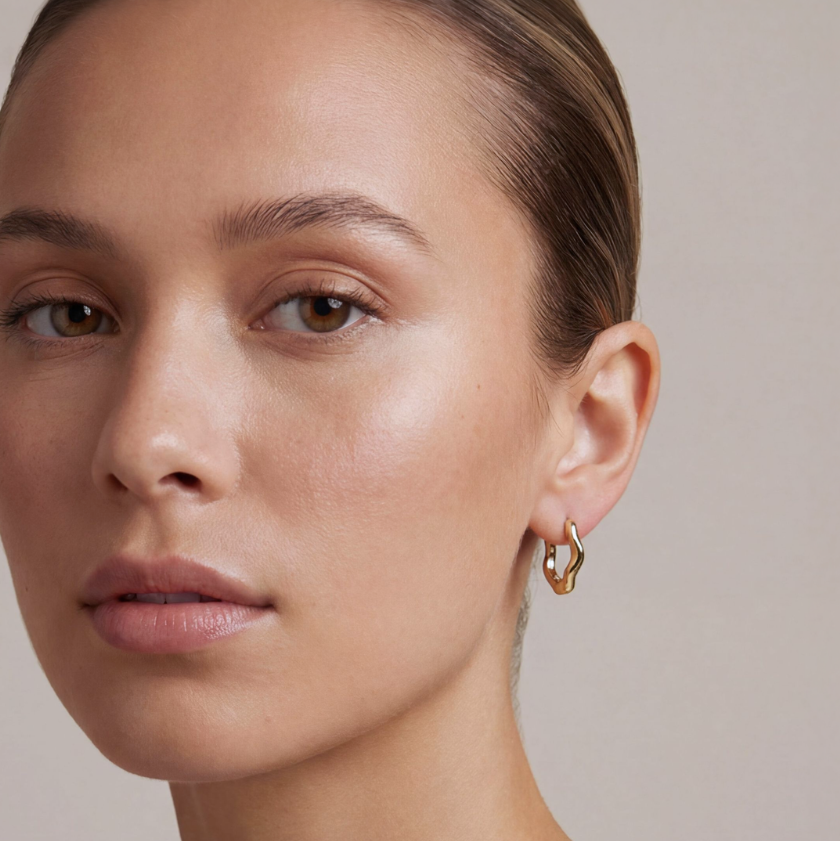 Close-up of a woman wearing gold hoop earrings against a neutral background