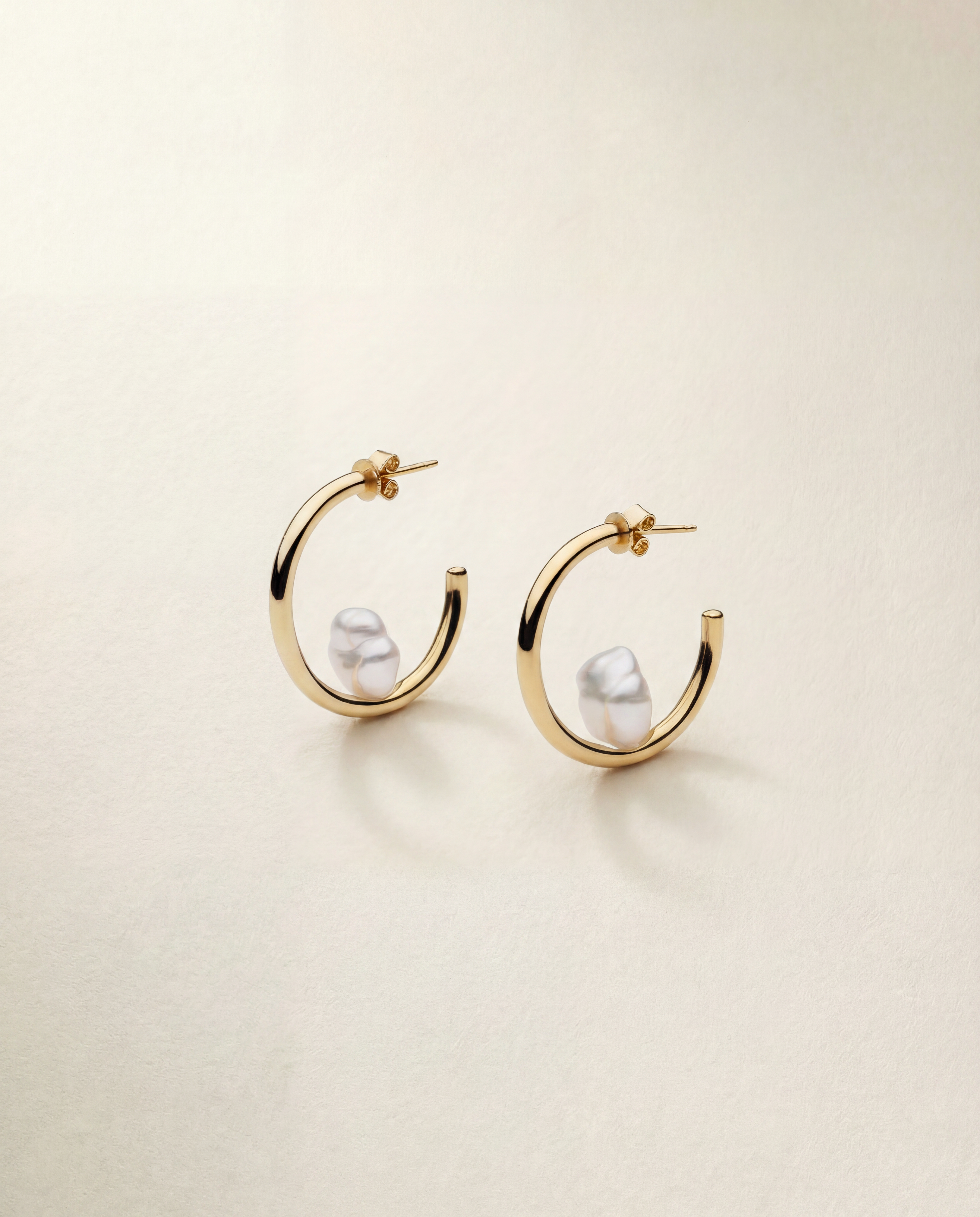 Gold hoop earrings with pearls on a beige background