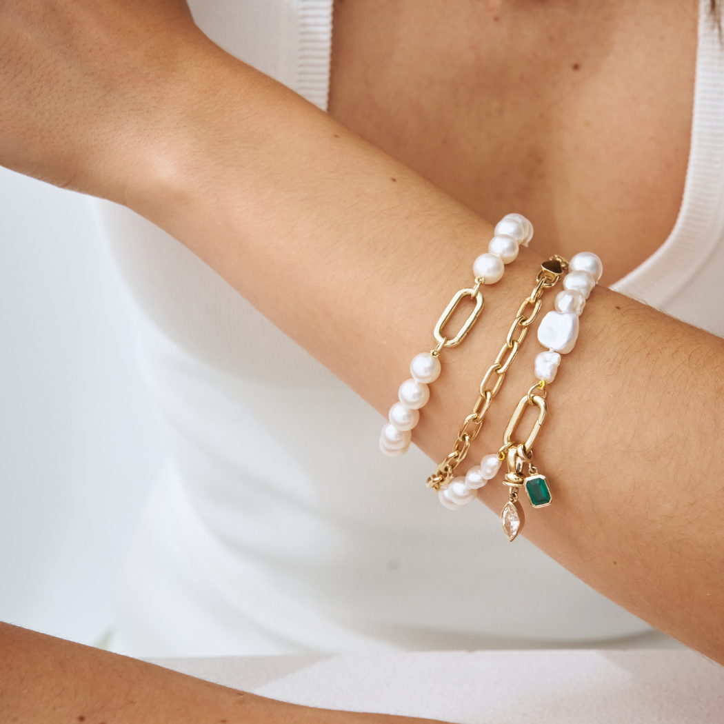 Up close of wrist wearing handmade South Sea Keshi pearl bracelets with 9k solid gold clasp with champagne diamond and emerald charm.