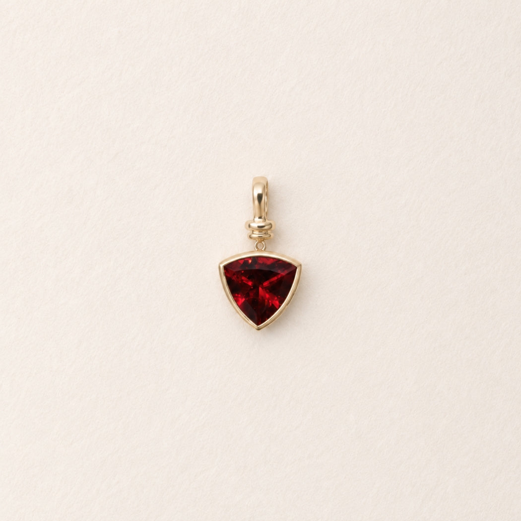 Gold pendant with a rubelite gemstone on a beige background
