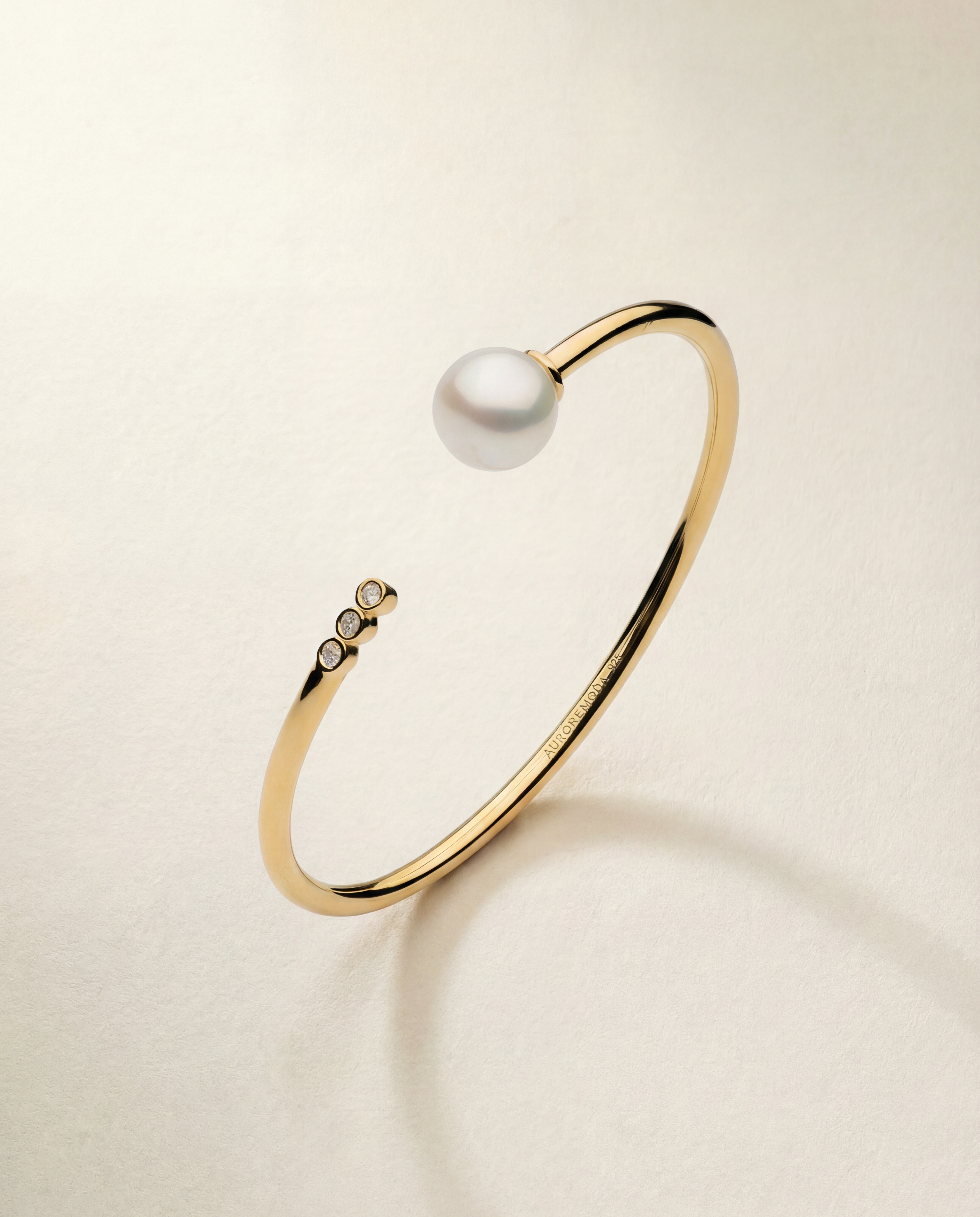 Gold bracelet with a pearl and small diamonds on a beige background