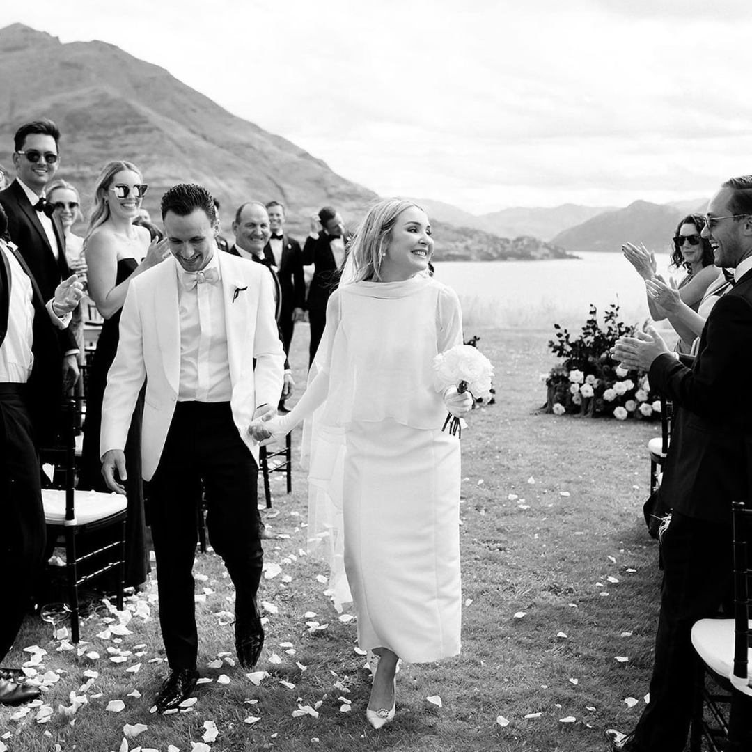 Bride and groom walking down the aisle at a lakeside wedding, wearing AUTORE MODA jewellery