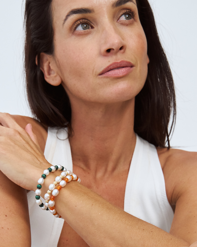 Woman wearing multiple beaded bracelets with alternating south sea pearls on her wrist against a light background