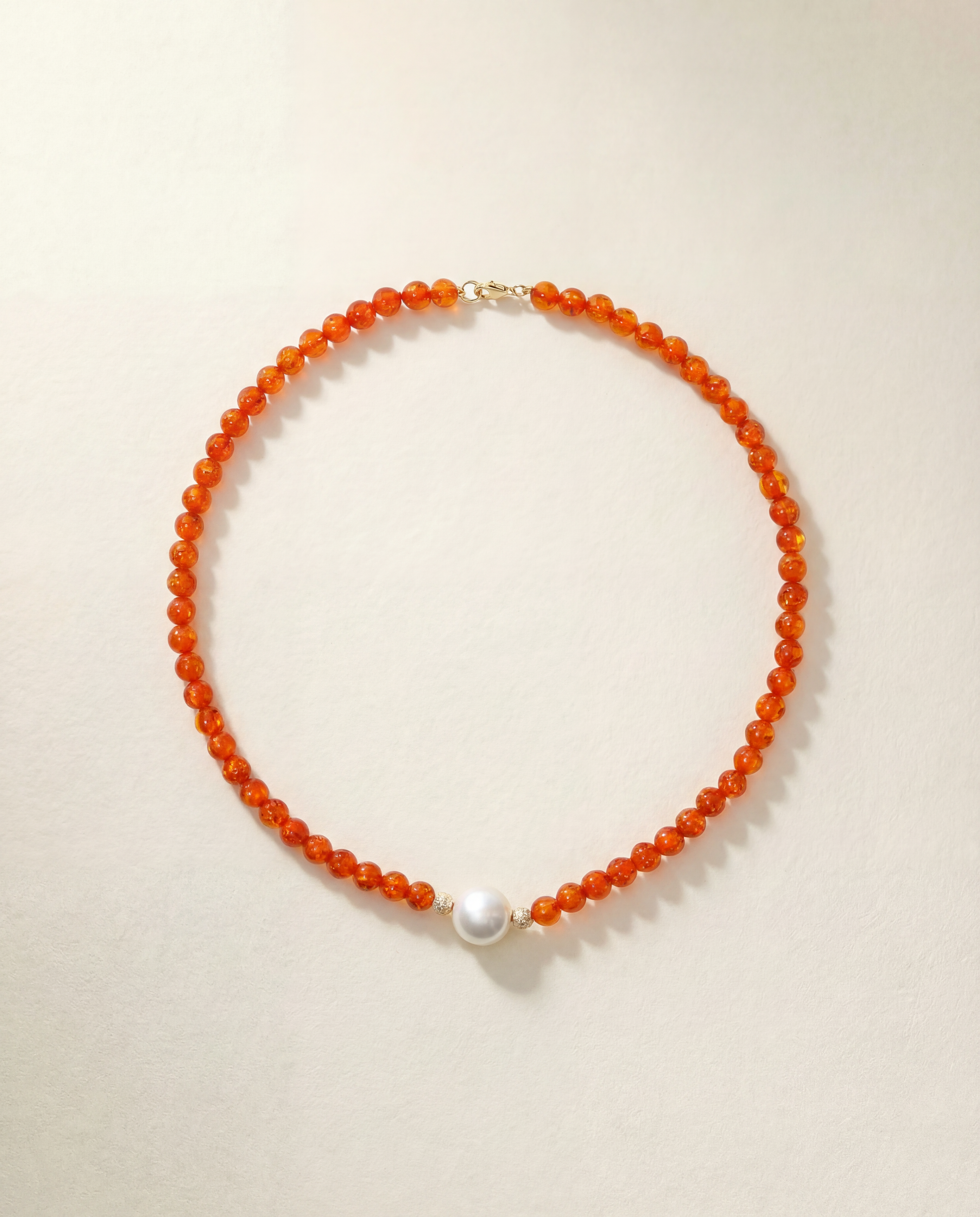 Necklace with orange beads and a pearl on a beige background