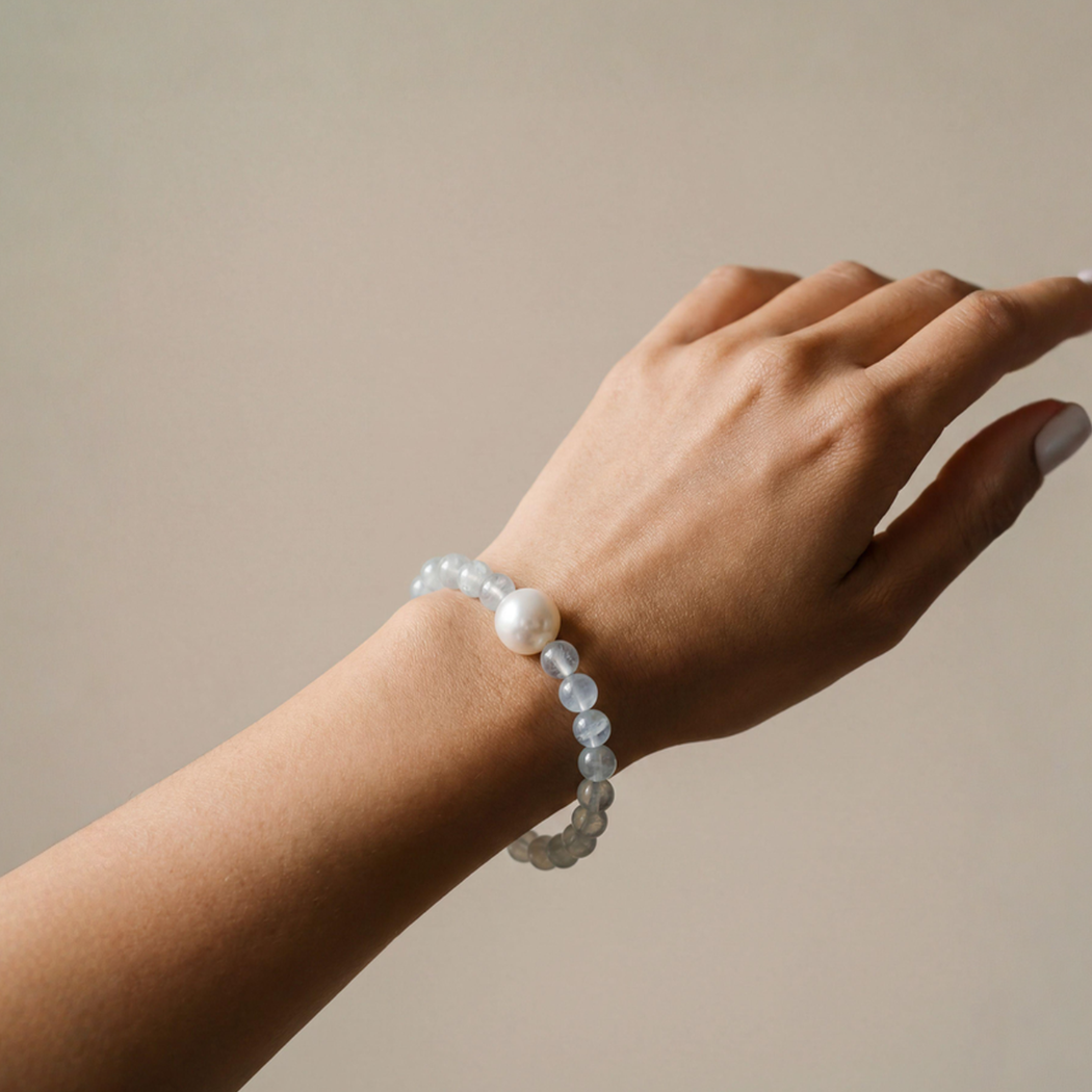 Hand wearing a pearl bracelet on a neutral background