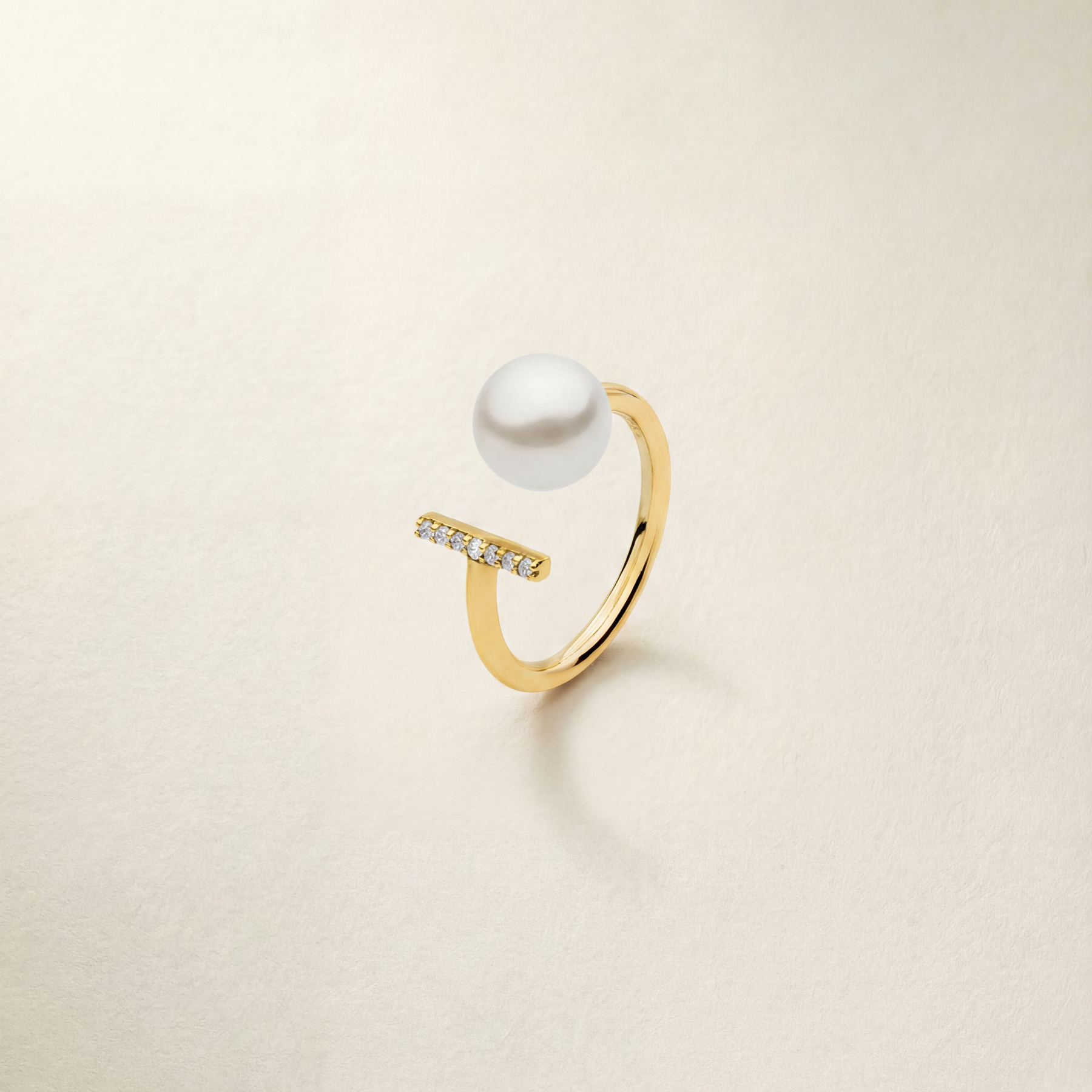 Gold ring with a pearl and small diamonds on a light beige background