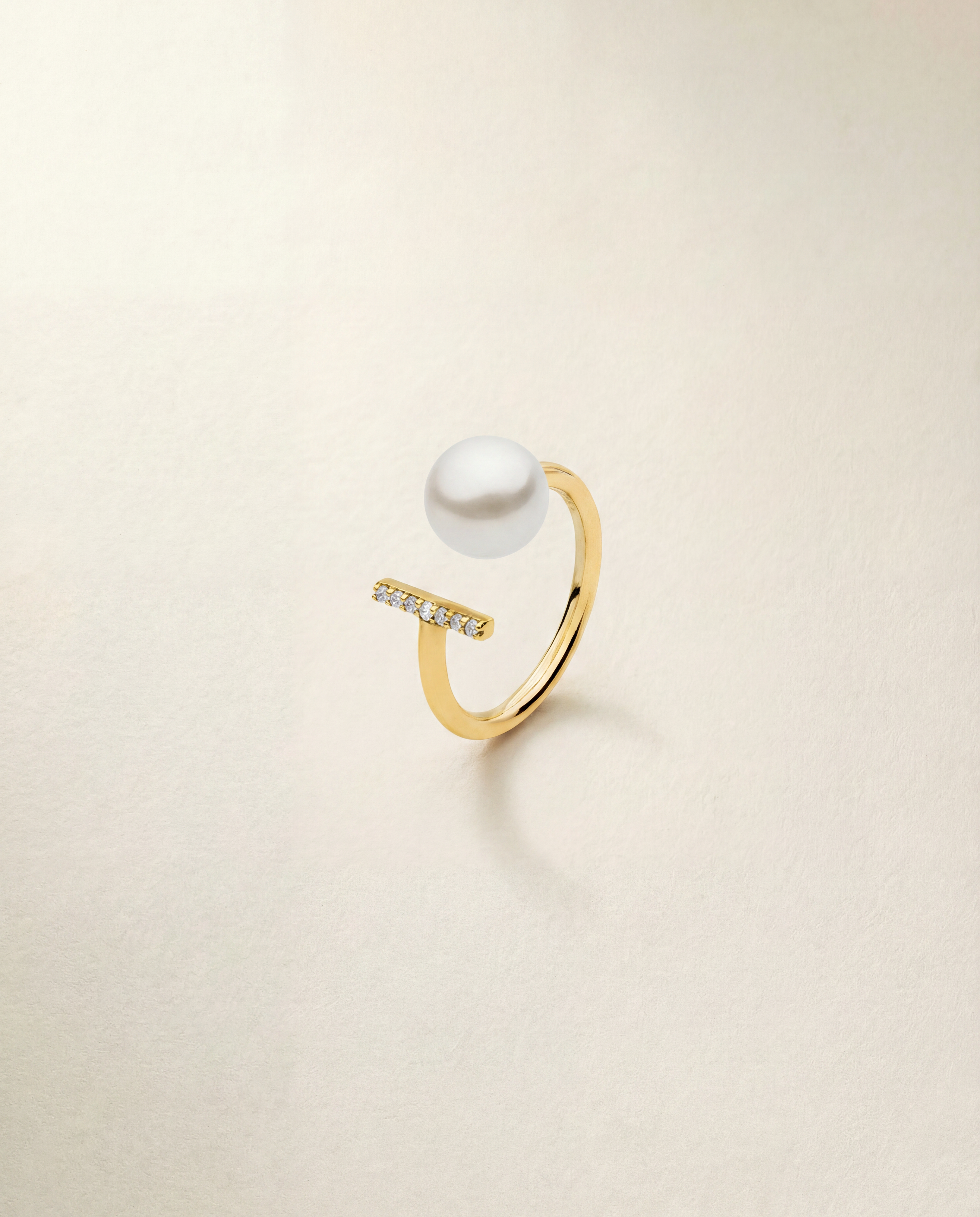 Gold ring with a pearl and small diamonds on a light beige background