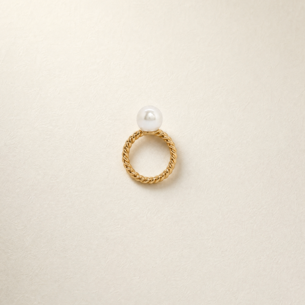 A gold ring with a twisted rope-style band and a single south sea white pearl at the top, photographed on a plain light background.