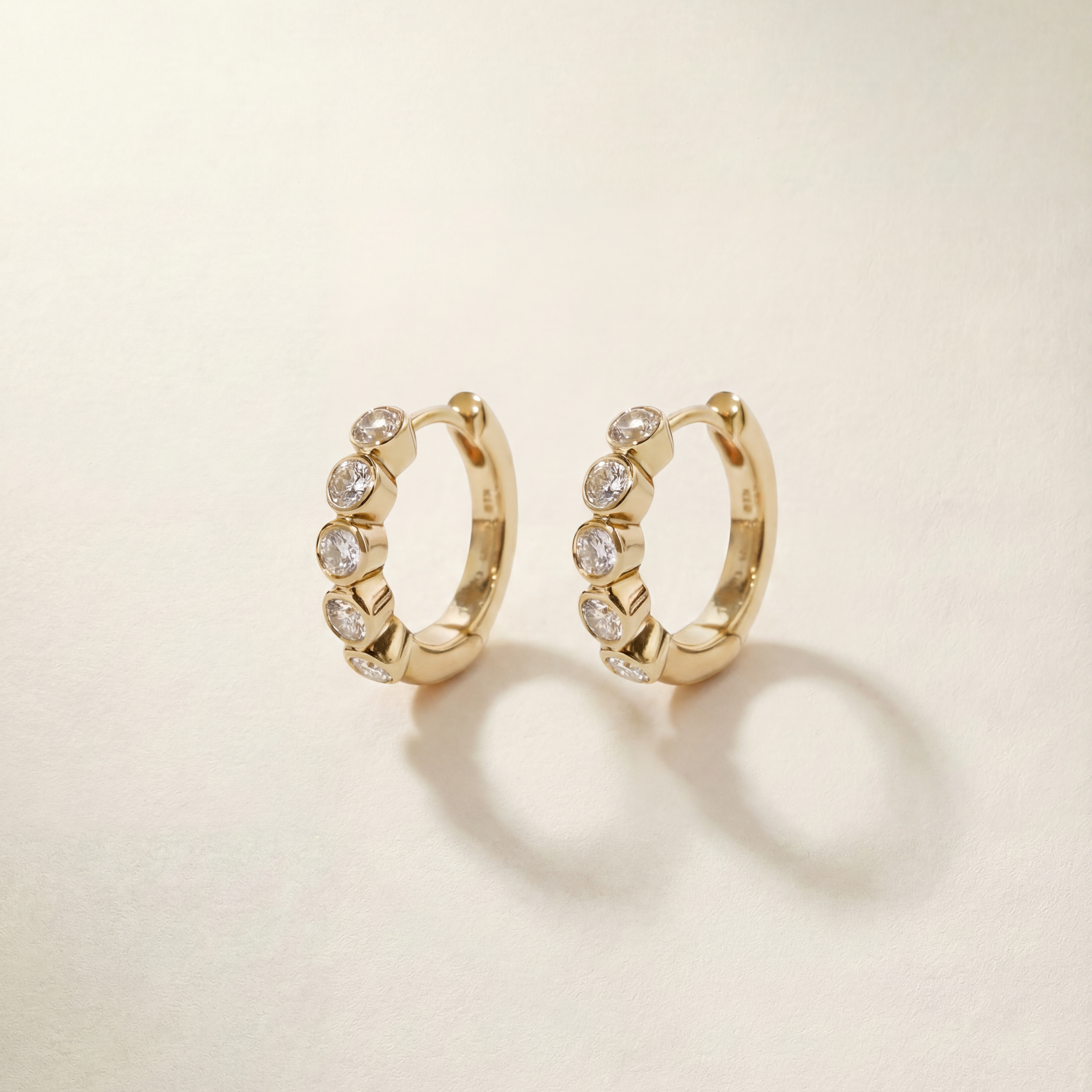 Gold hoop earrings with embedded stones on a beige background