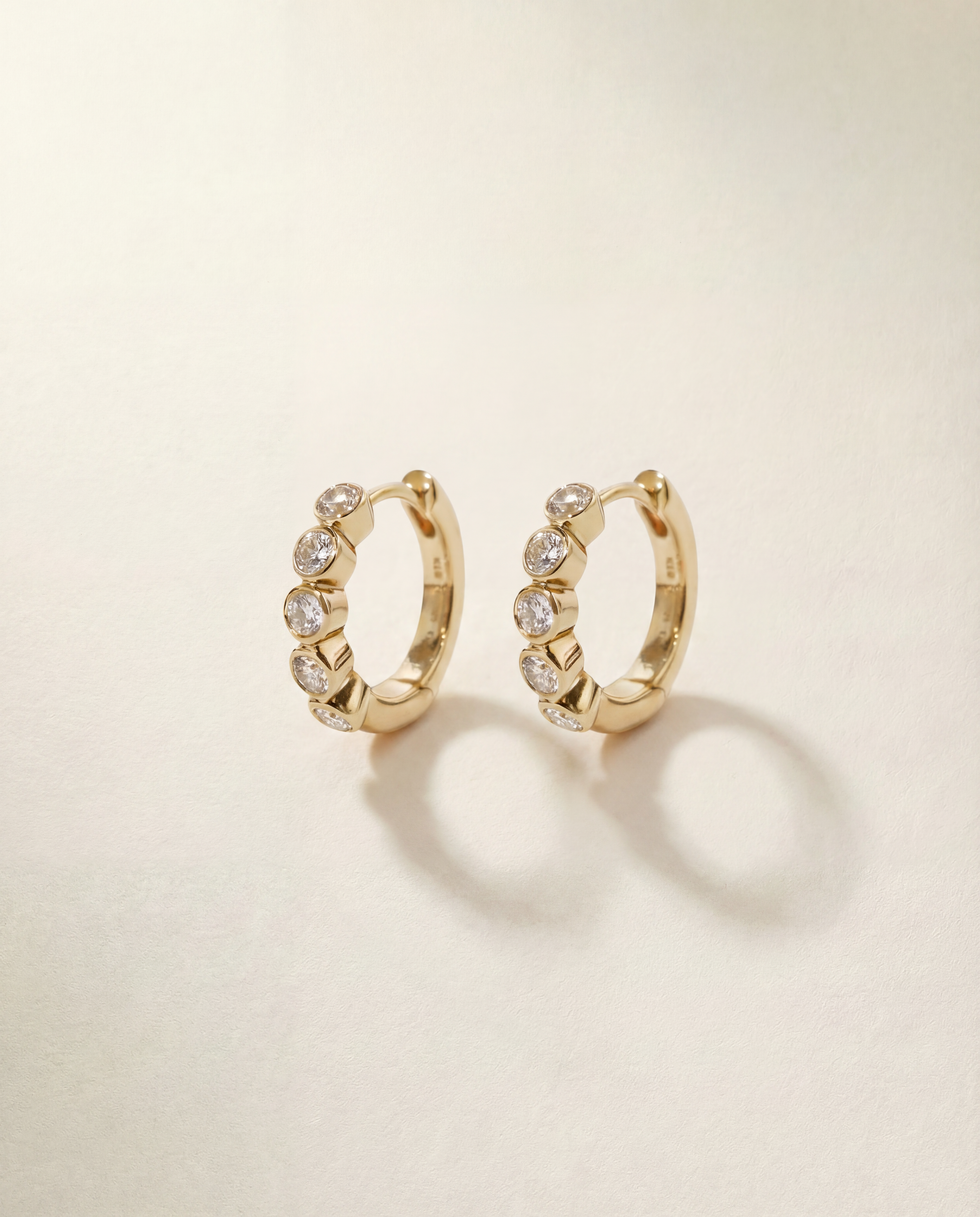 Gold hoop earrings with embedded stones on a beige background