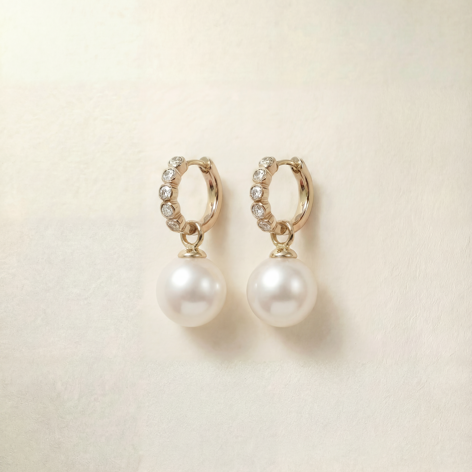 Pair of pearl earrings with gold hoop accents on a beige background