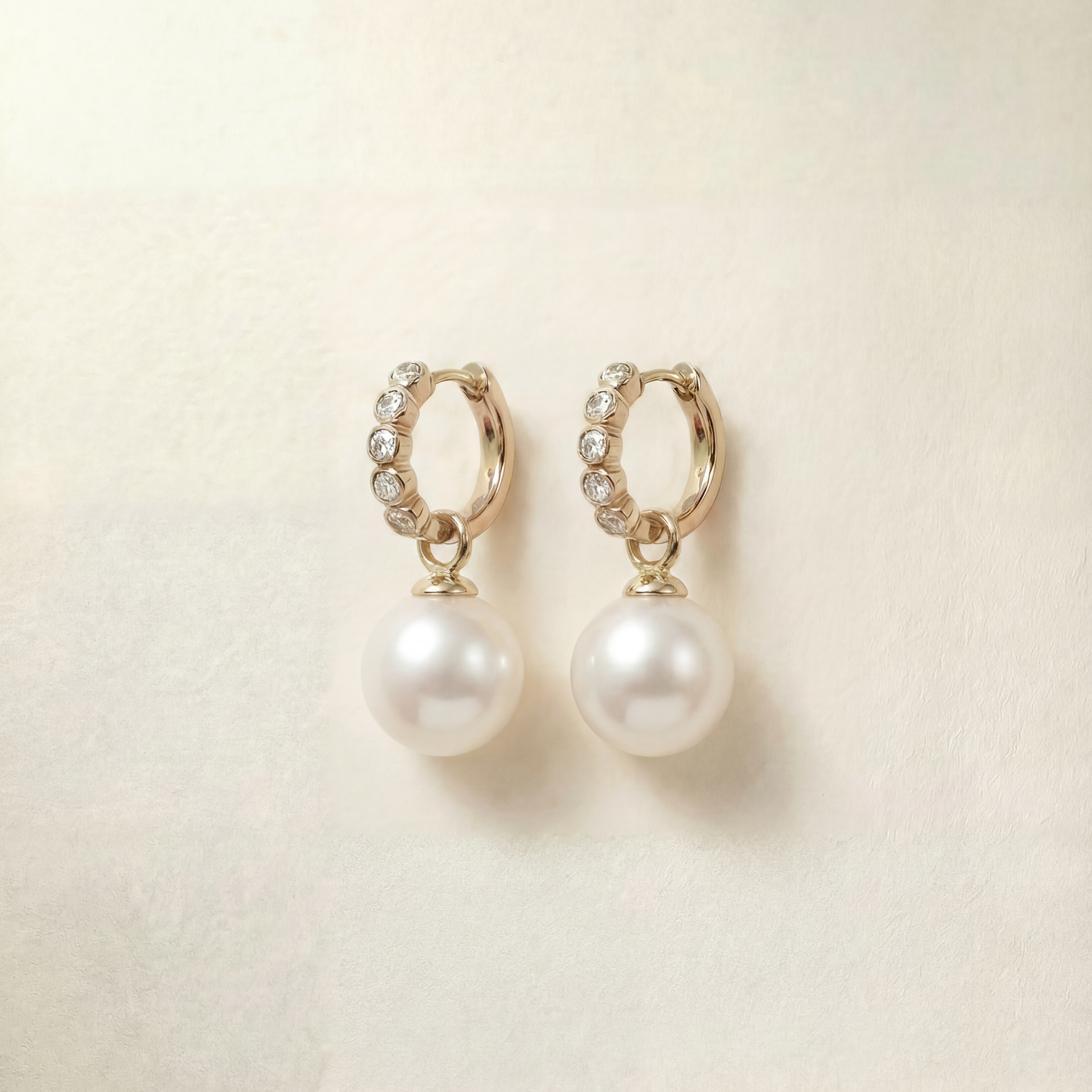 Pair of pearl earrings with gold hoop accents on a beige background