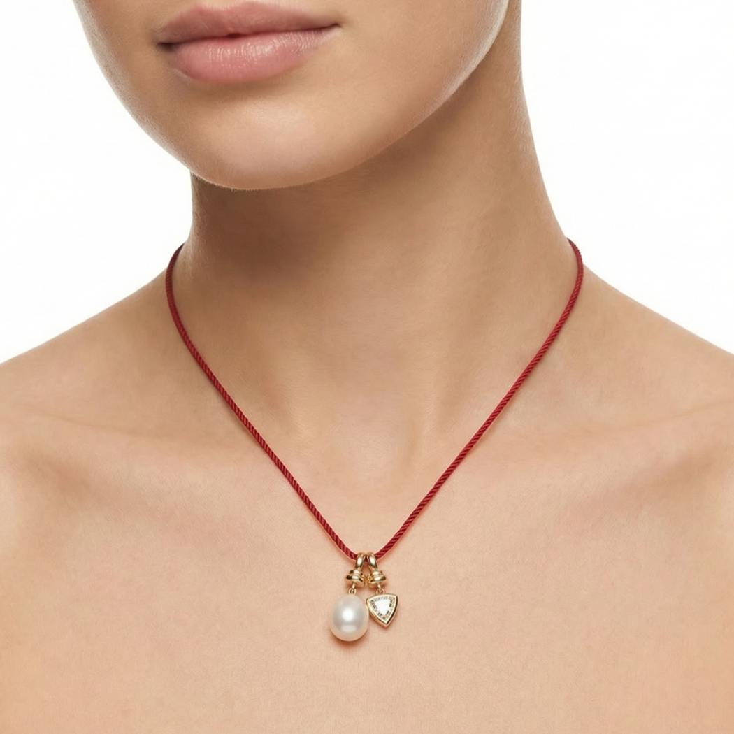 Necklace with a pearl pendant and heart charm on a red cord, worn by a person.