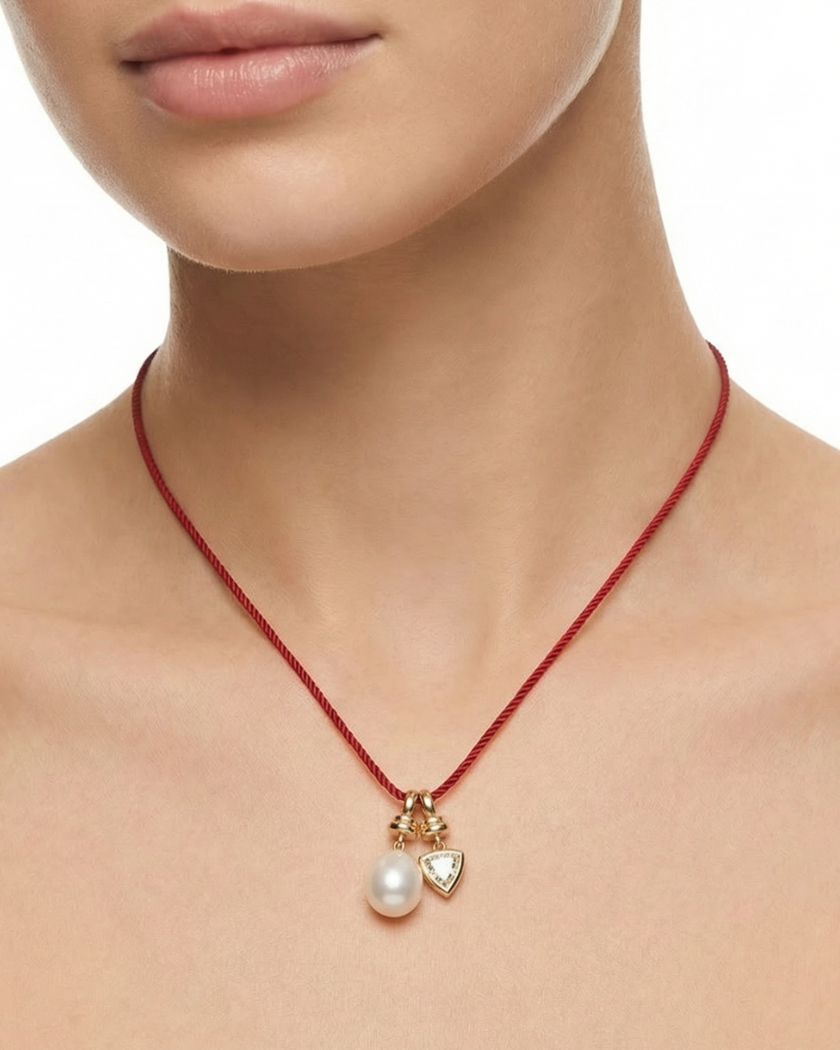 Necklace with a pearl pendant and heart charm on a red cord, worn by a person.