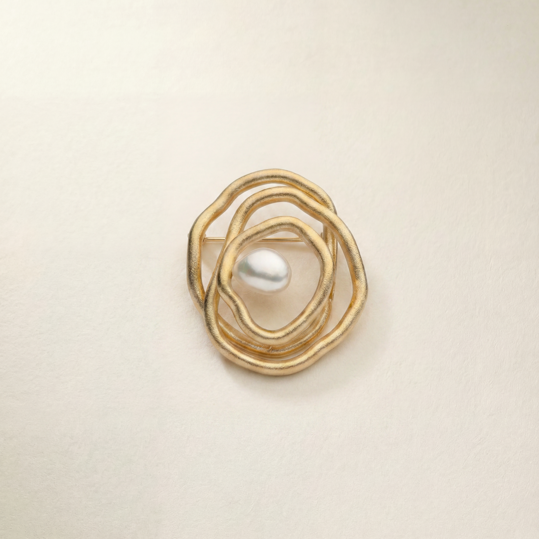 Gold brooch with a pearl on a beige background