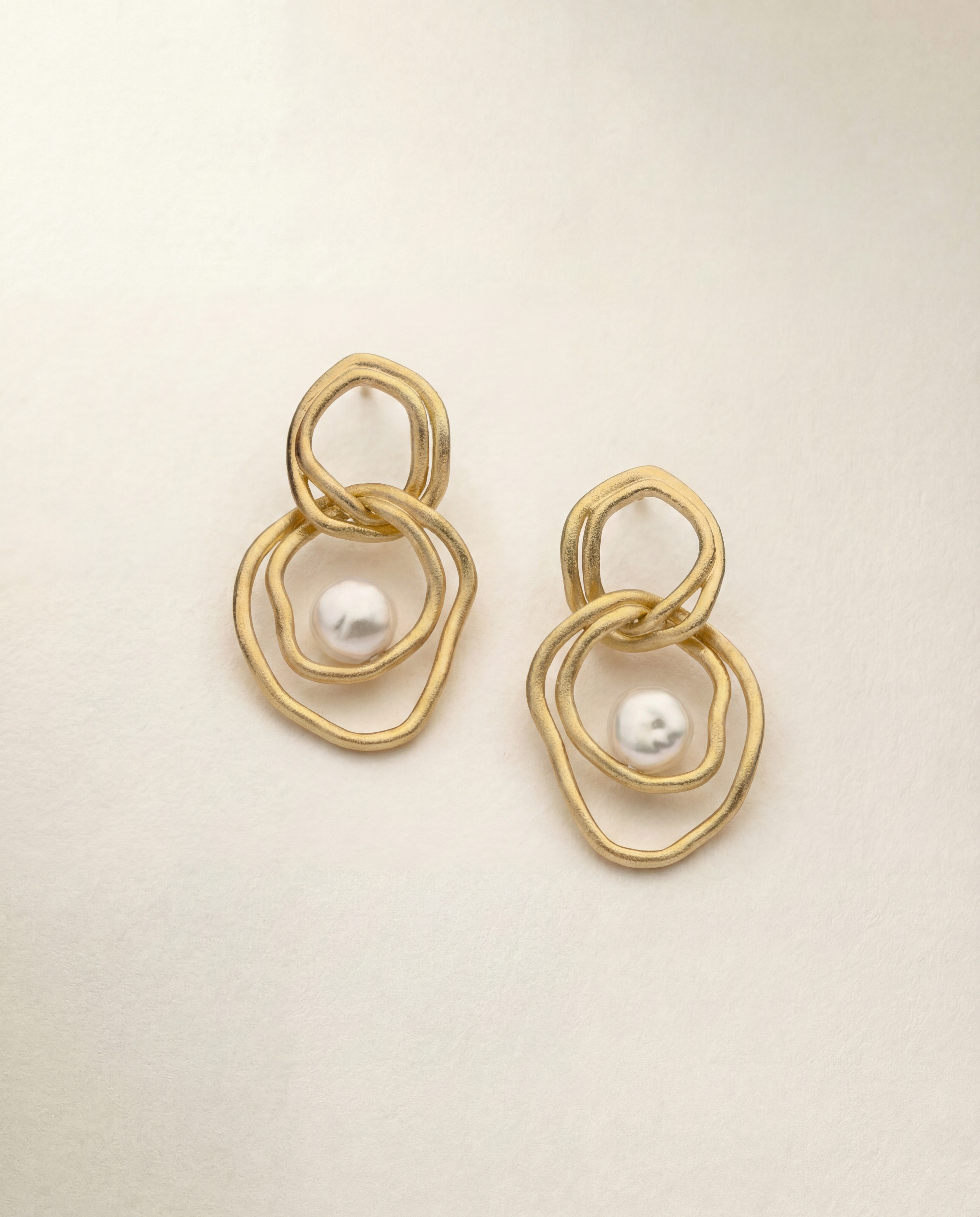 Gold earrings with pearl centers on a beige background