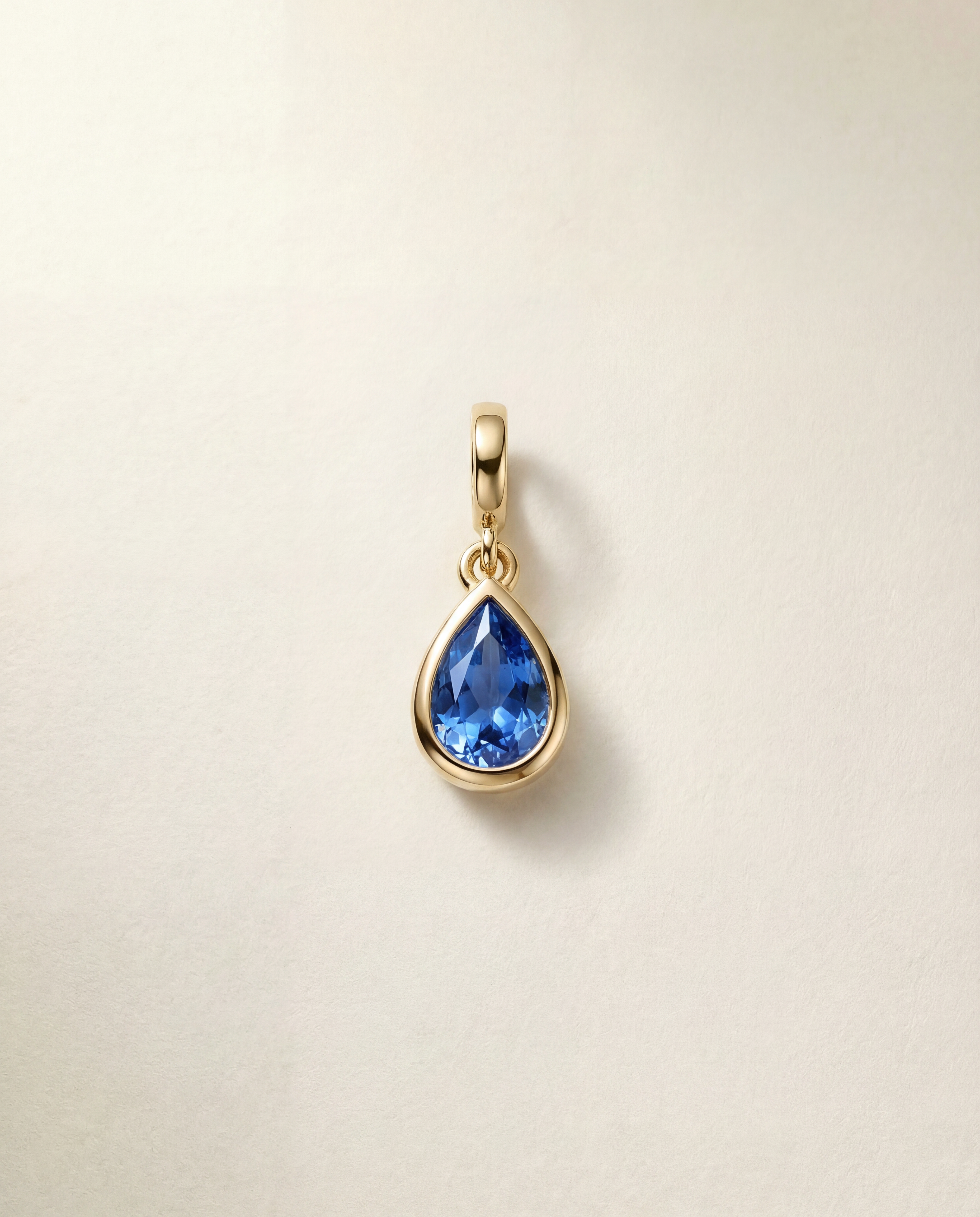 Gold pendant with a blue gemstone on a beige background