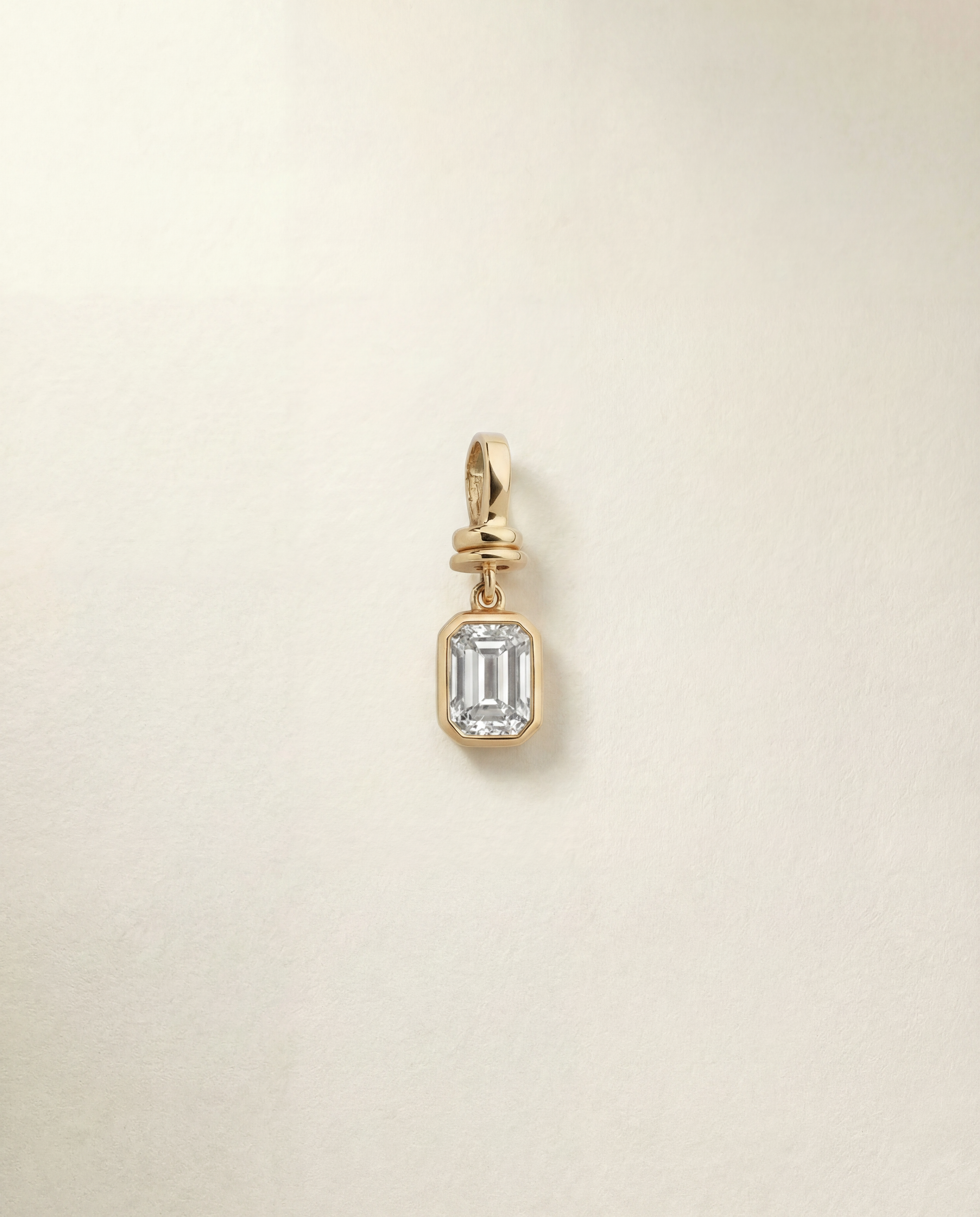 Gold pendant with a emerald diamond on a beige background